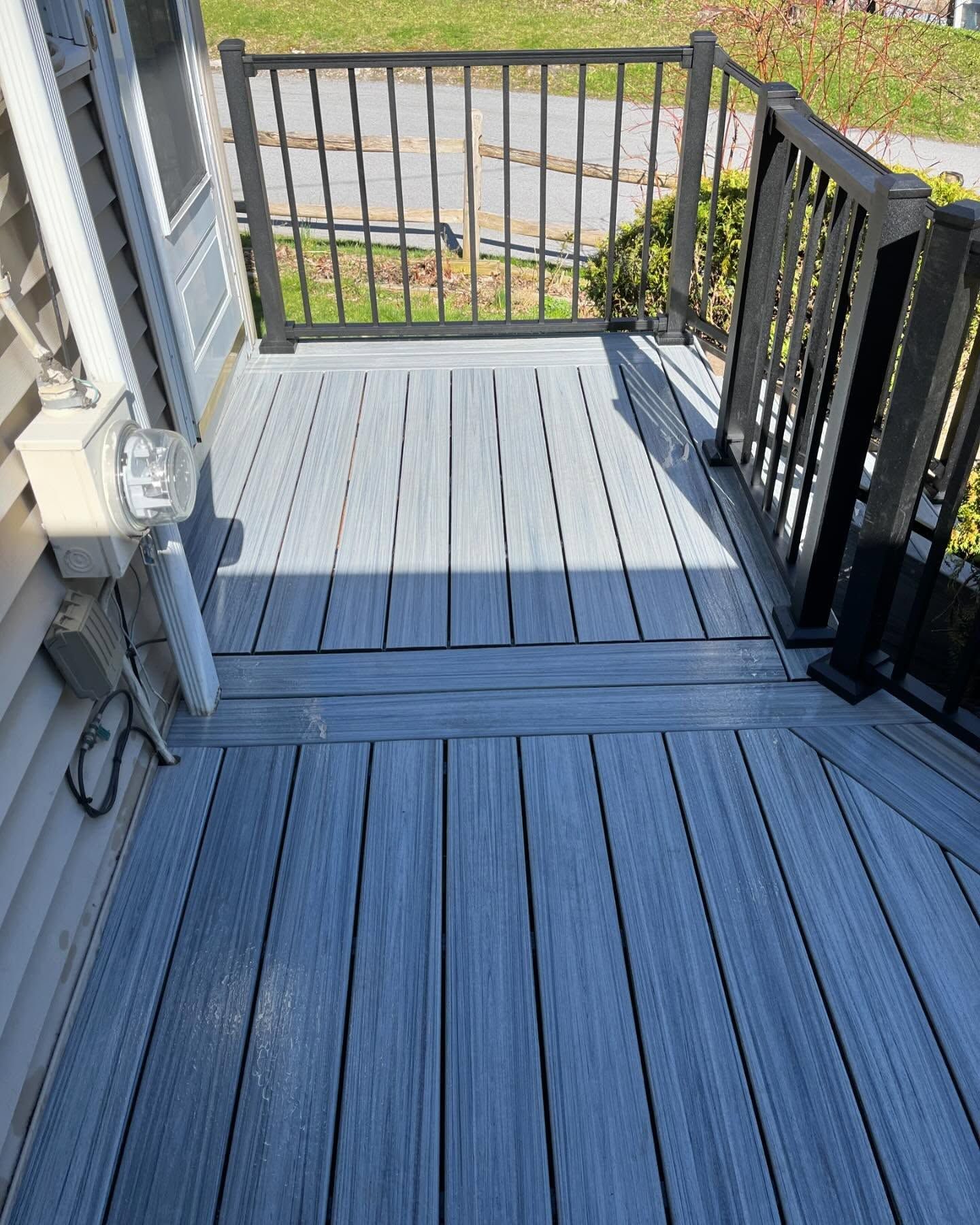 Gray composite deck with black railing, attached to a light-colored house, next to a small yard.