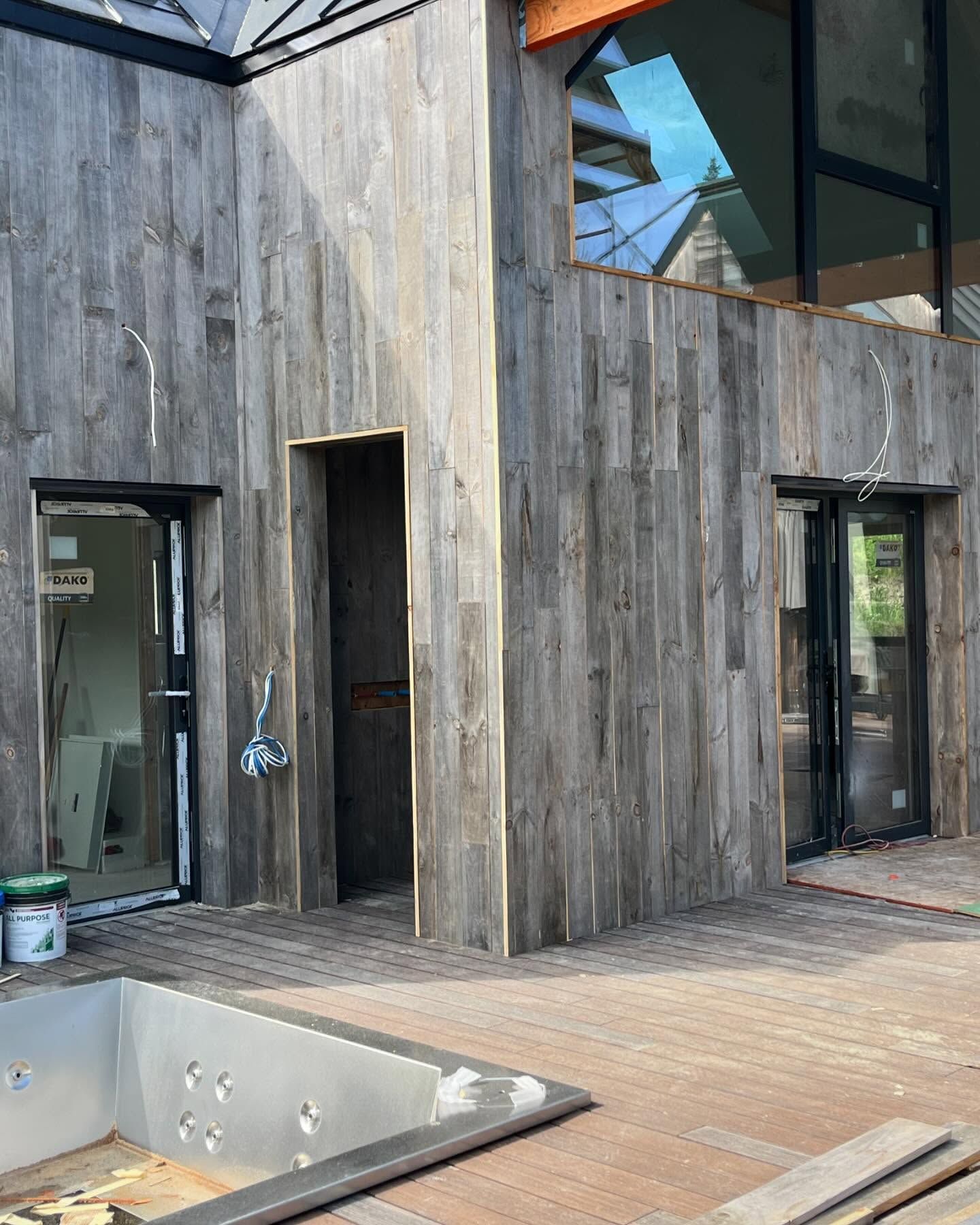 Exterior building with weathered wood siding, open doorway, hot tub, and modern windows.