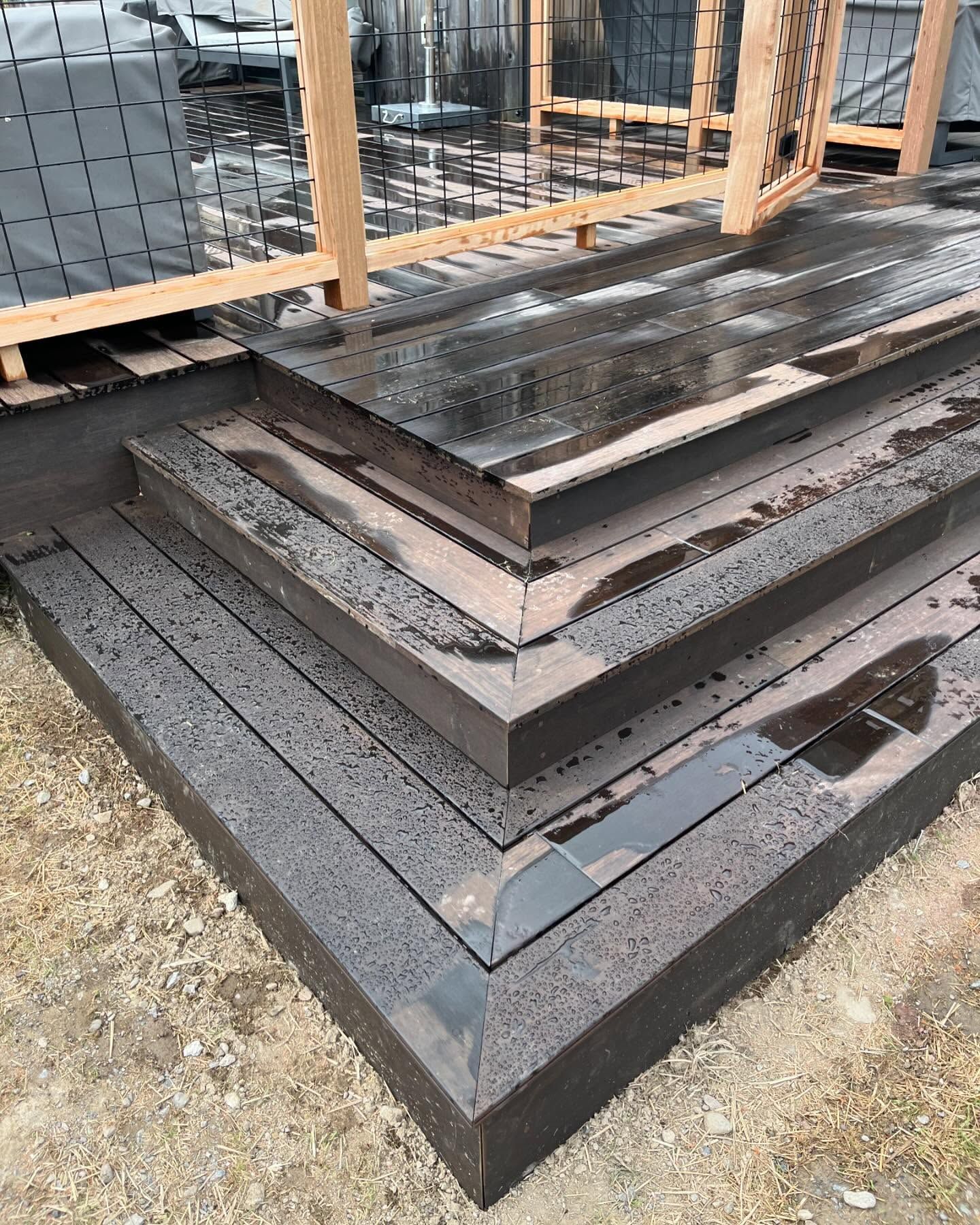 Composite deck steps with dark brown boards, wet from rain.