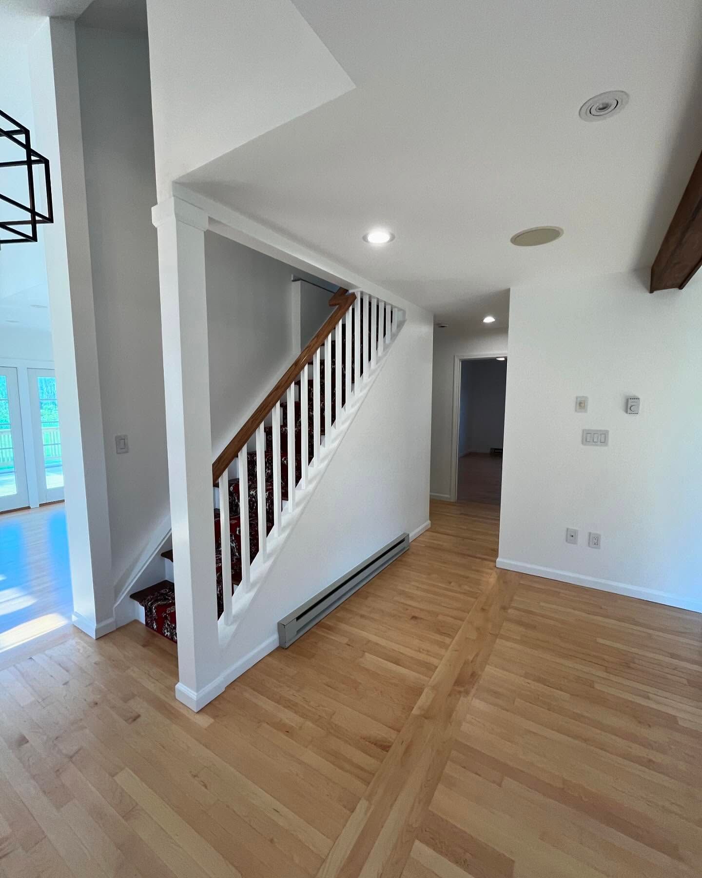 Interior view of a foyer with stairs, wood floors, and white walls.