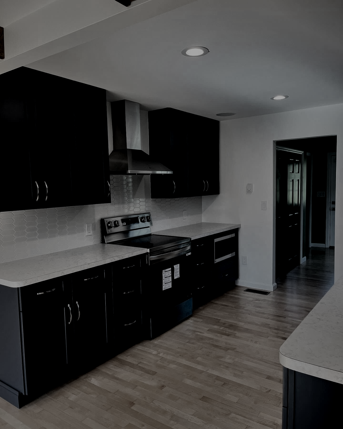 Black kitchen cabinets and appliances, stainless steel range hood, white countertops, and light wood floors.