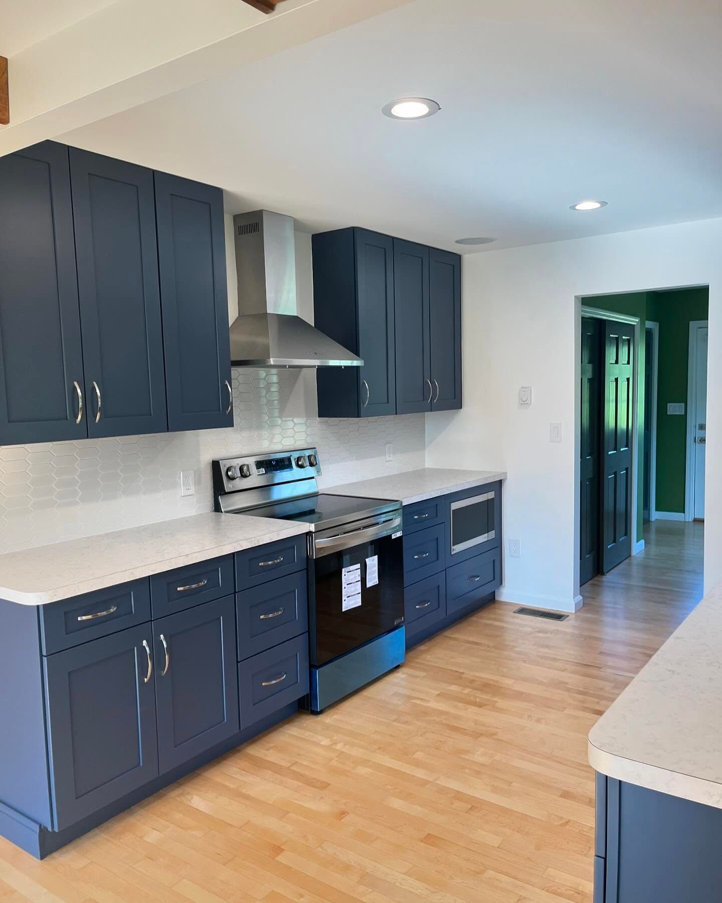Navy blue kitchen cabinets, white countertops, stainless steel appliances, and light wood floors.