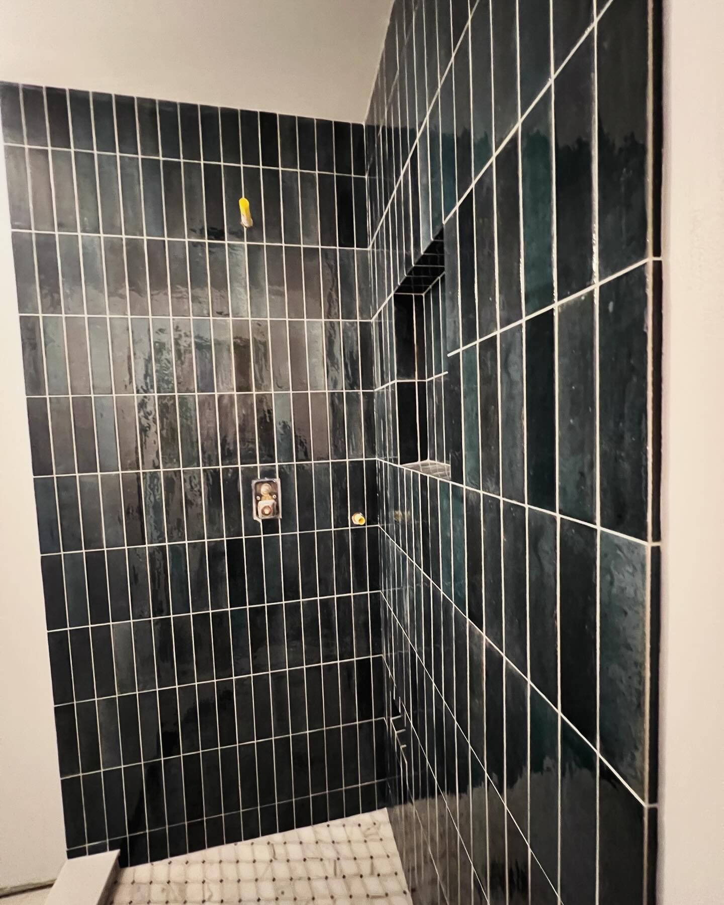 Dark tiled shower with a recessed shelf and fixtures installed.