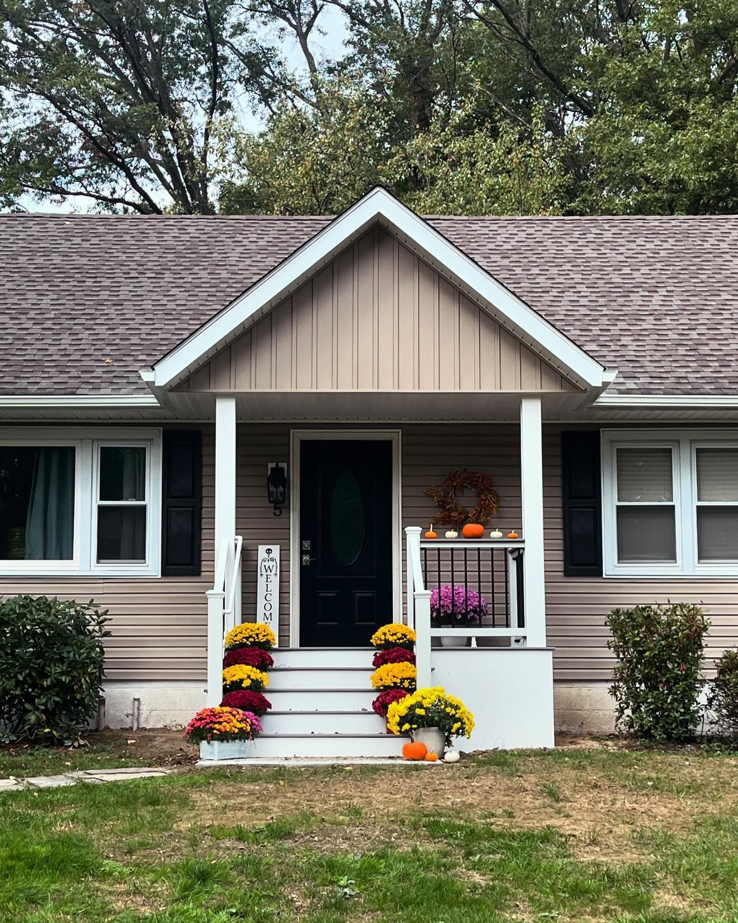 Curb appeal of a tan house decorated with fall mums and pumpkins.