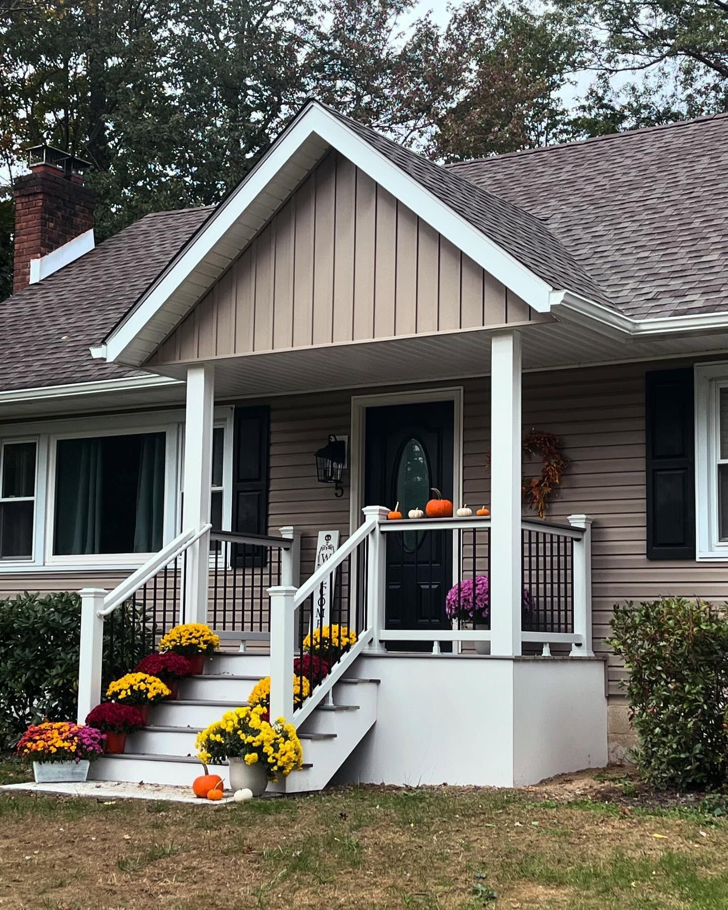 A tan house with a porch decorated with autumn mums.