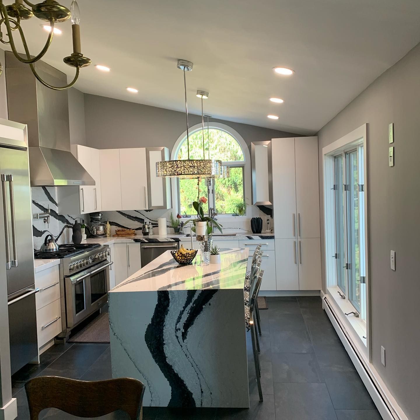 Modern kitchen with white cabinets, marble countertops, and a central island with a decorative light fixture.