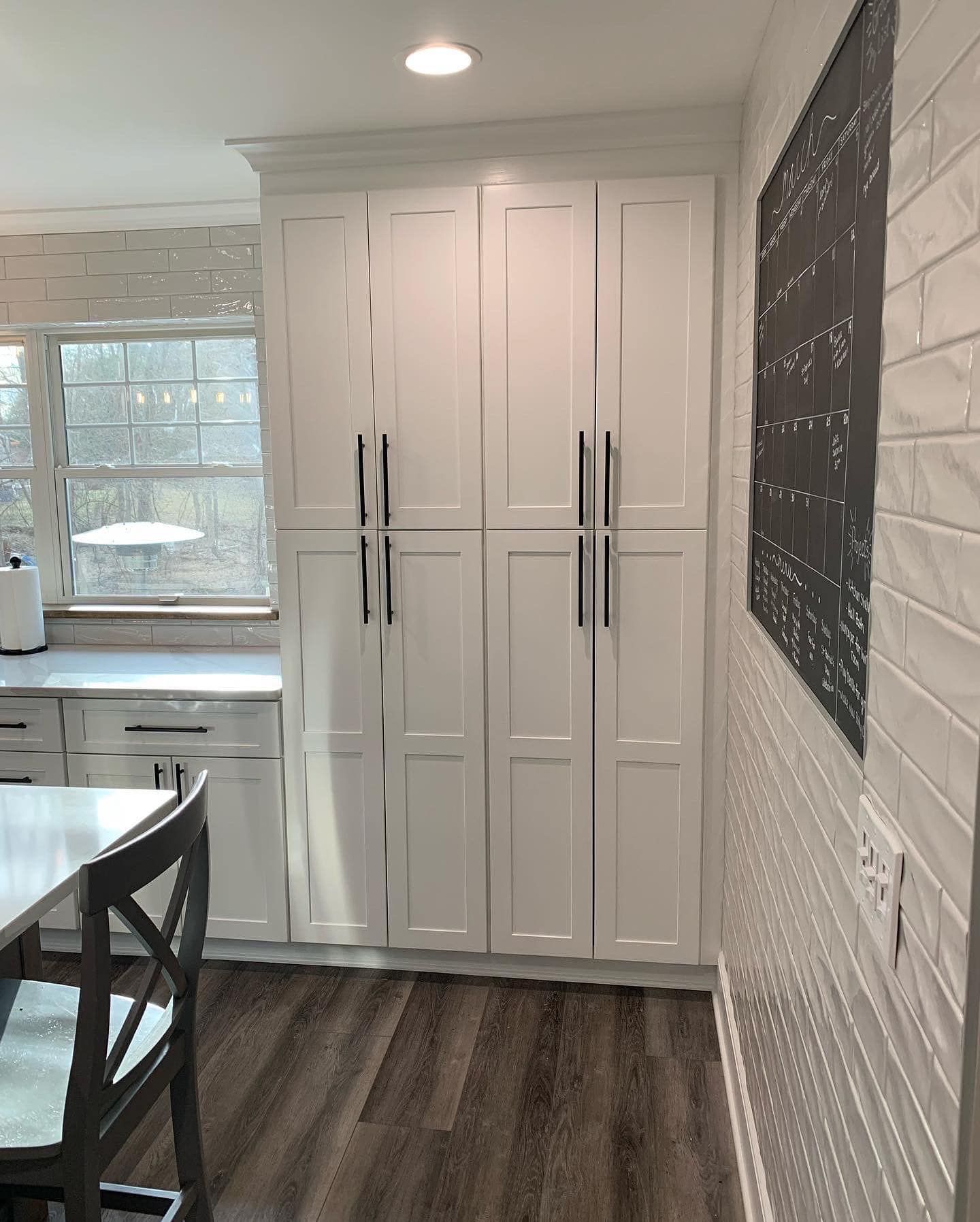 White pantry cabinets in a kitchen with dark handles, wood floor, and a chalk board on the wall.