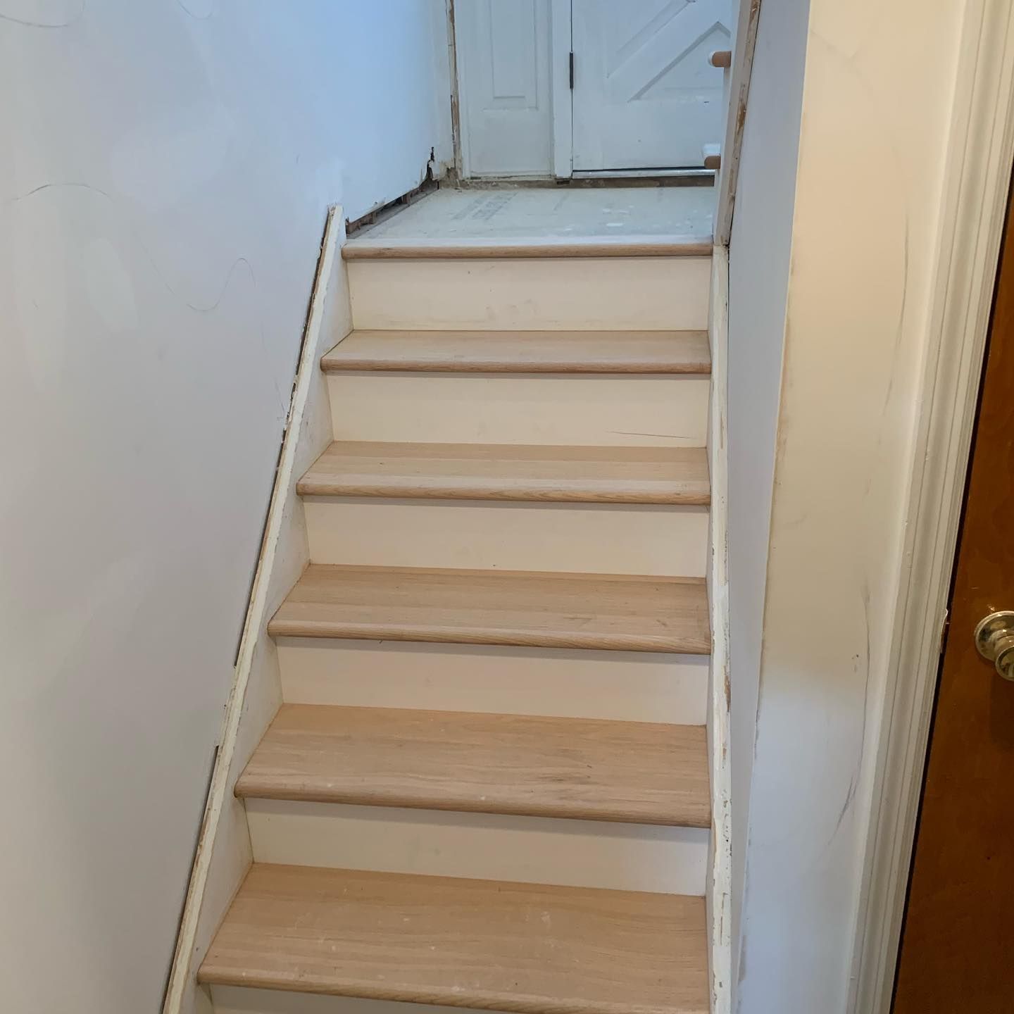Staircase with white risers and natural wood treads, leading to a door at the top.