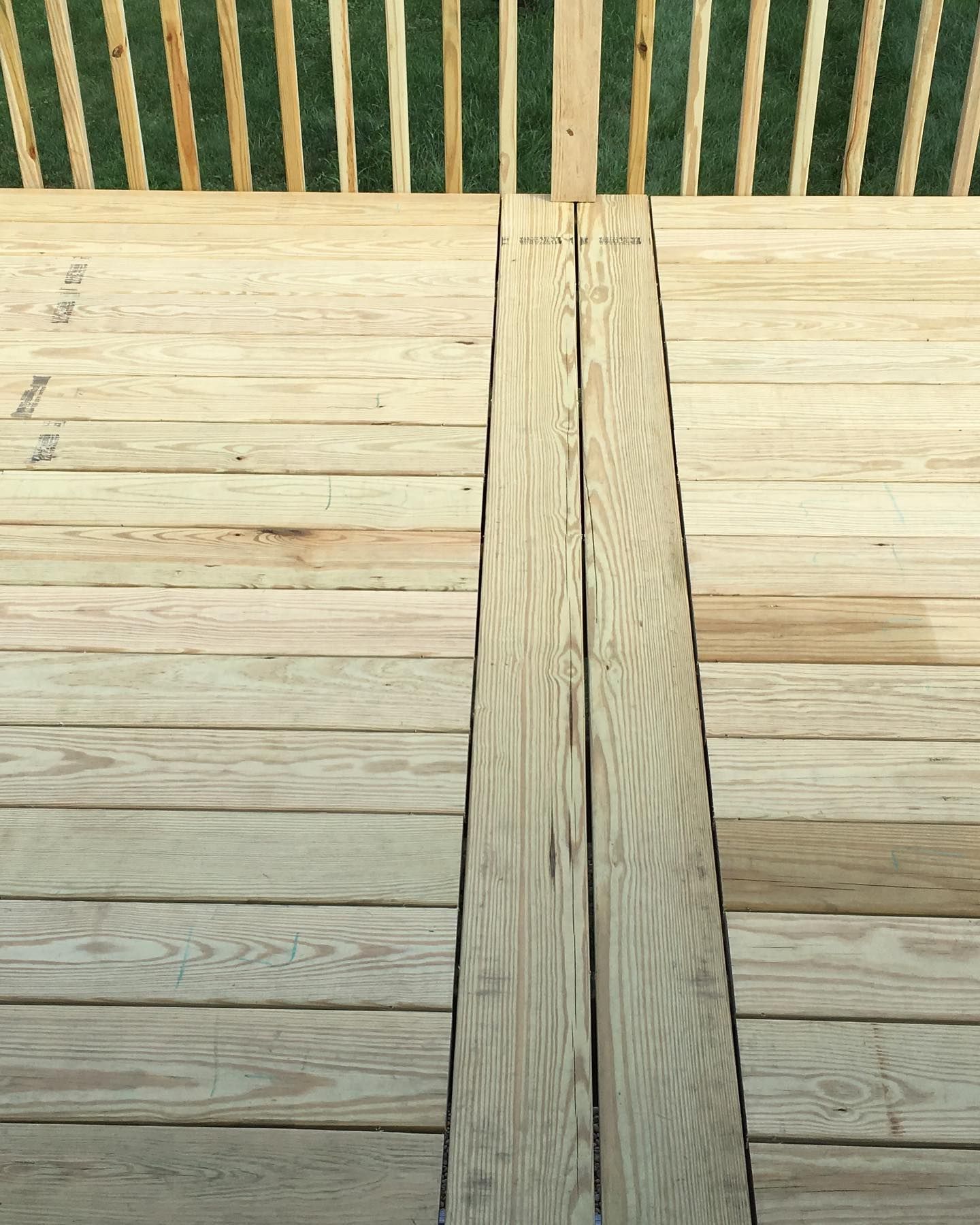 Wooden planks forming a surface, two planks raised in the center, against a striped green background.