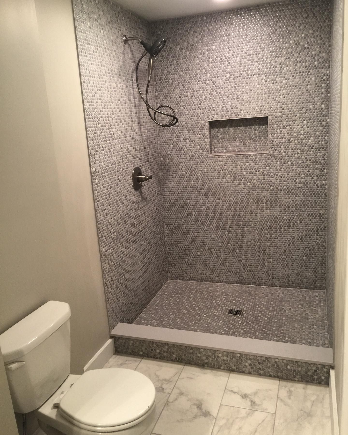 Small bathroom with gray tiled shower, marble floor, and white toilet.