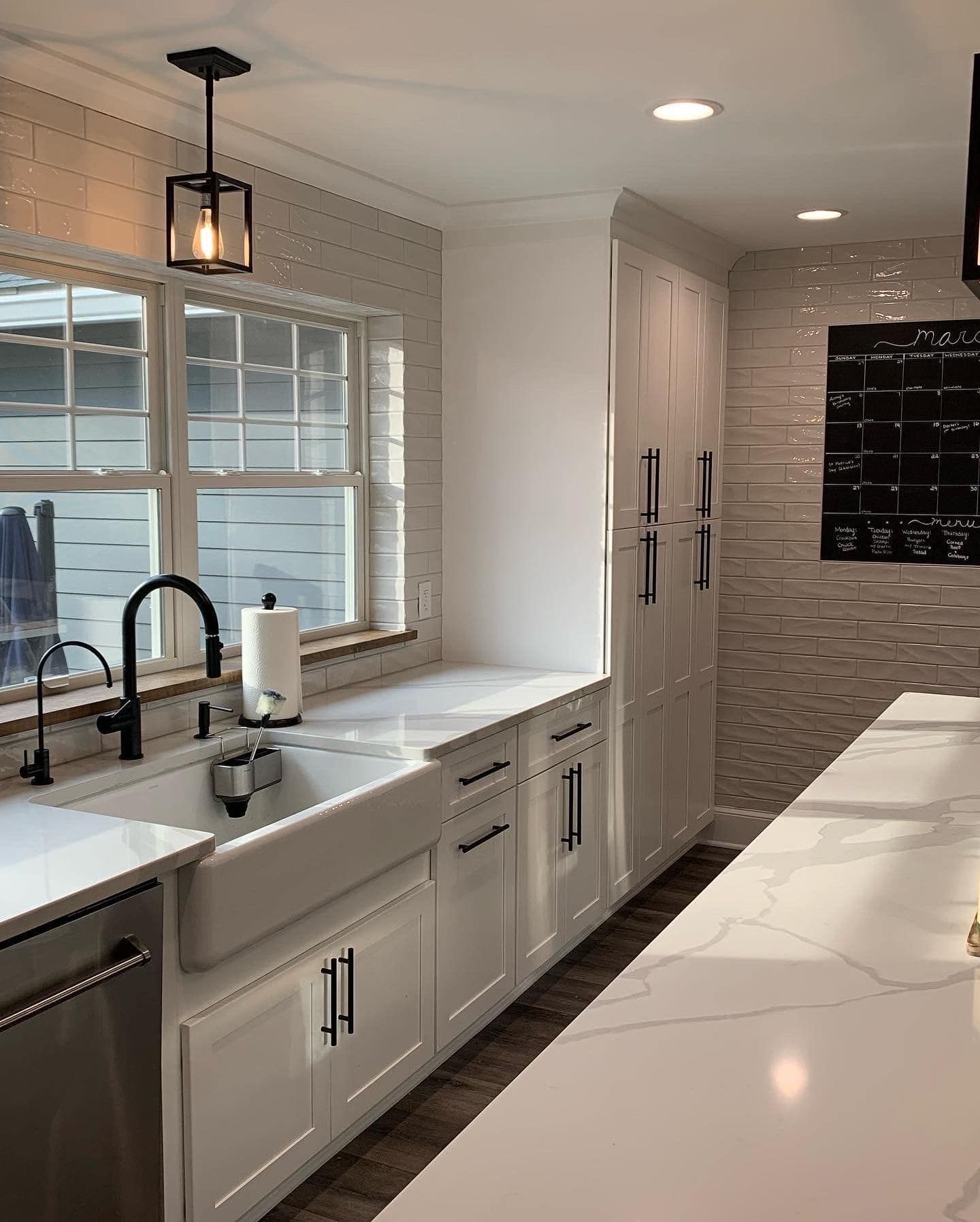 White kitchen with farm sink, black hardware, and modern light fixture.