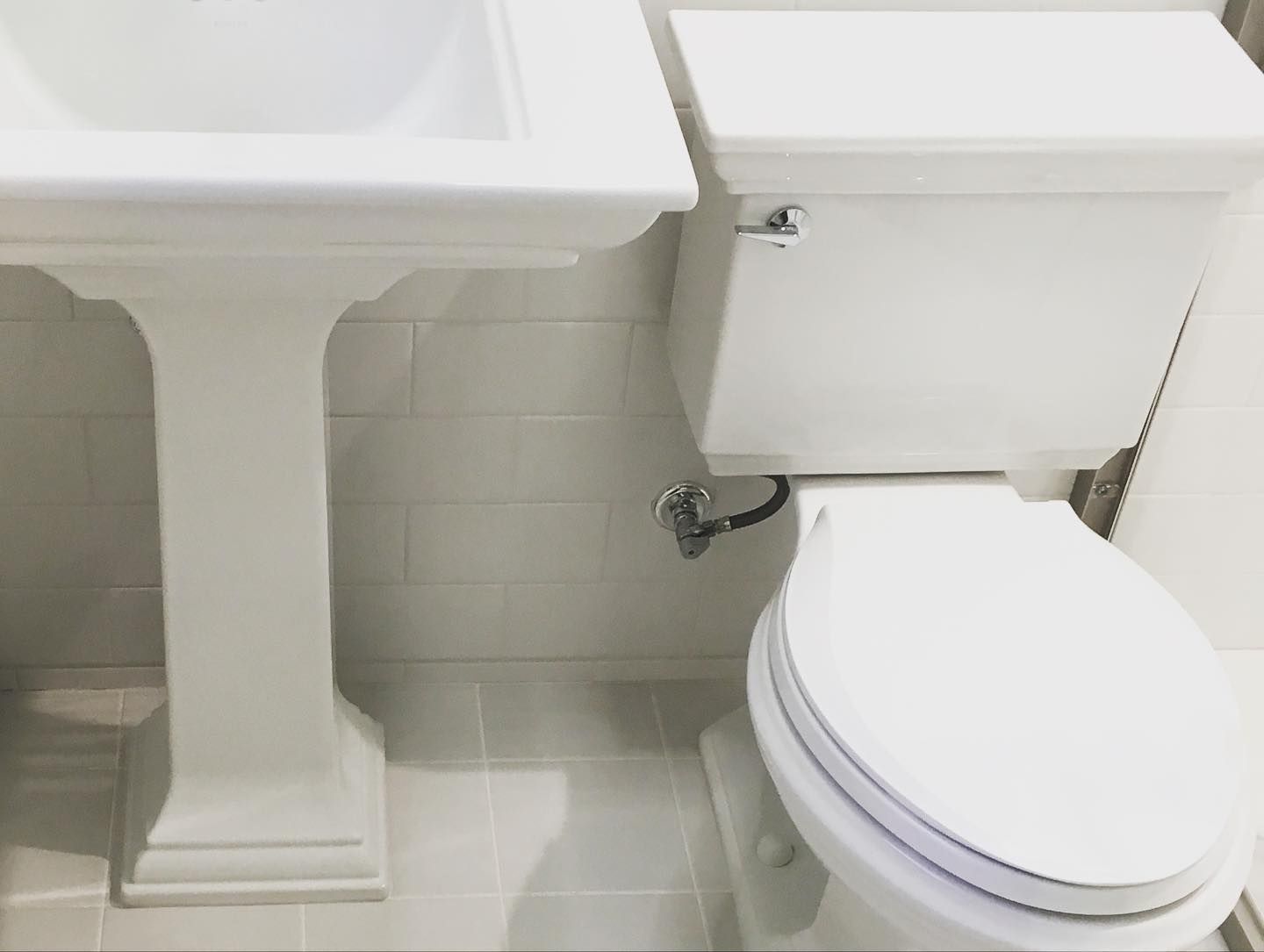 White pedestal sink next to a white toilet in a tiled bathroom.