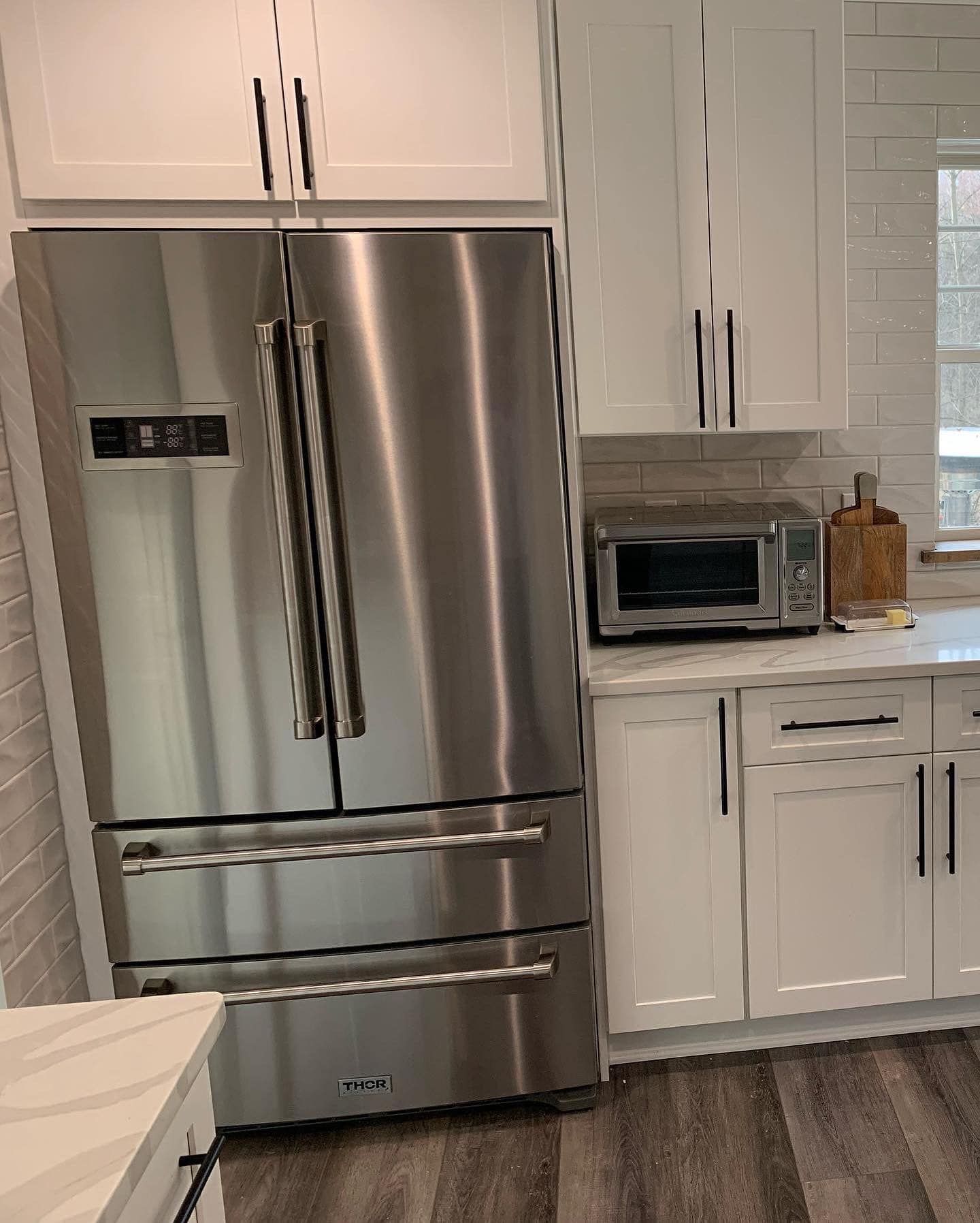 Stainless steel refrigerator in a white kitchen with cabinets and countertop.