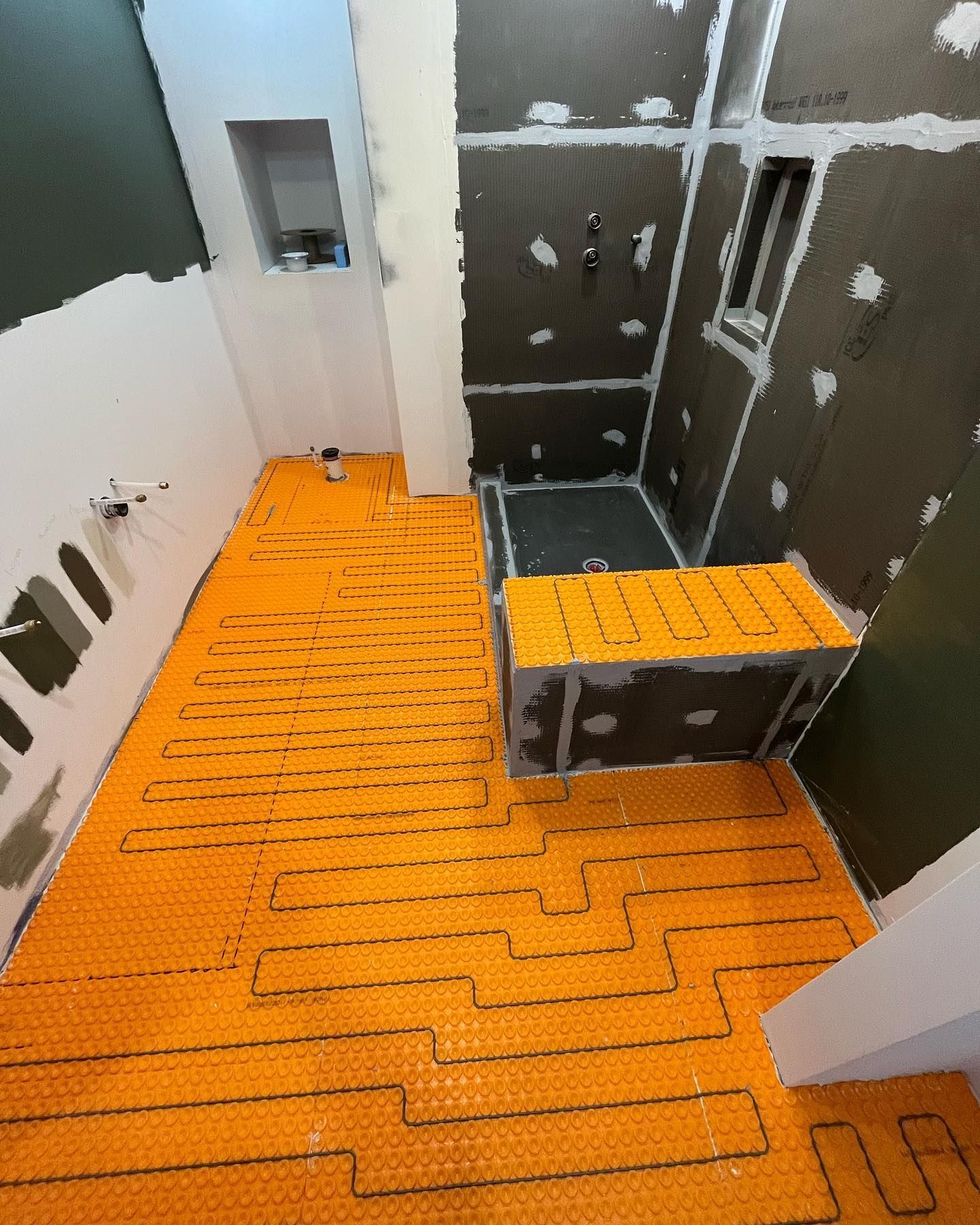 Bathroom under construction with orange heated floor mat. Dark gray walls and shower base.