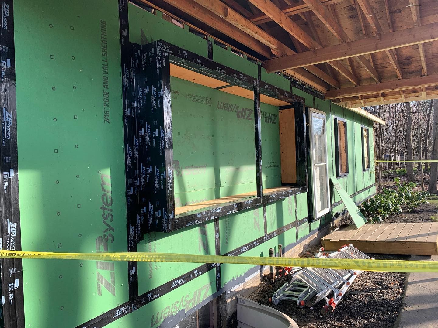 Exterior wall of a house under construction, green siding, black tape around a window, yellow caution tape in foreground.