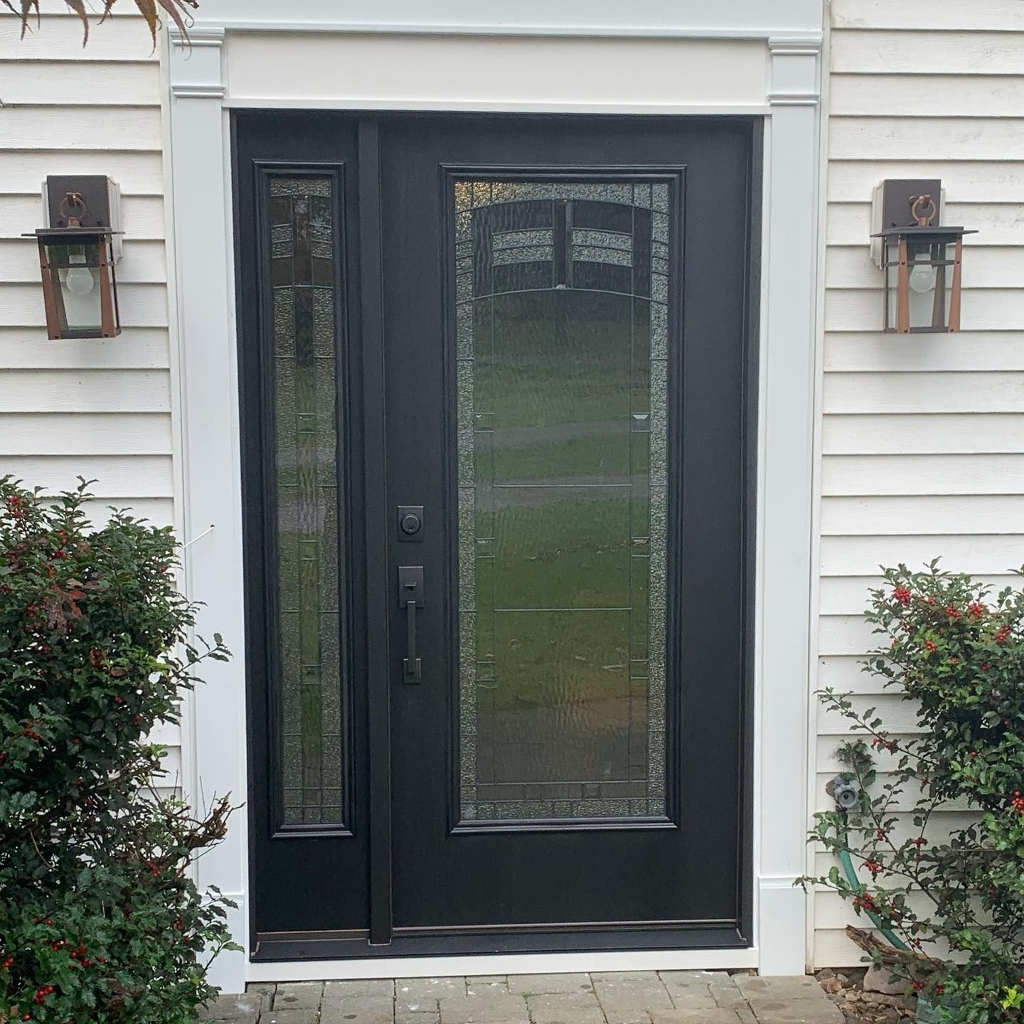 Black front door with glass panels and sidelight, white trim, and sconces on a white clapboard house.