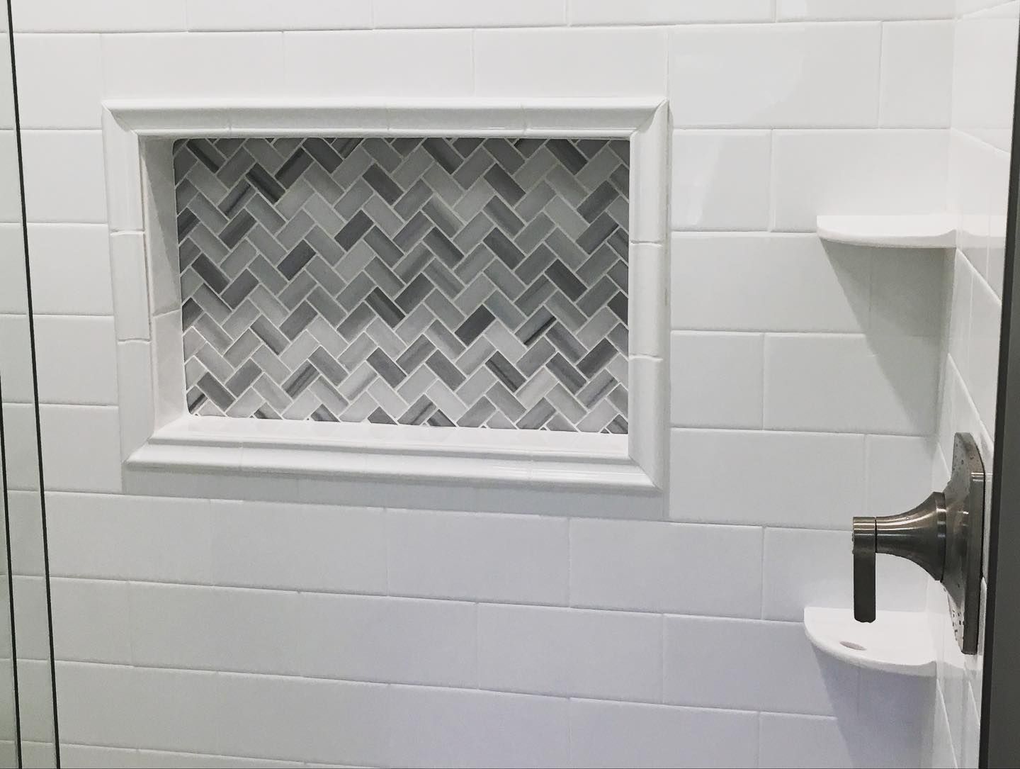 White tiled shower with a gray and white herringbone tile niche, and a white soap ledge.