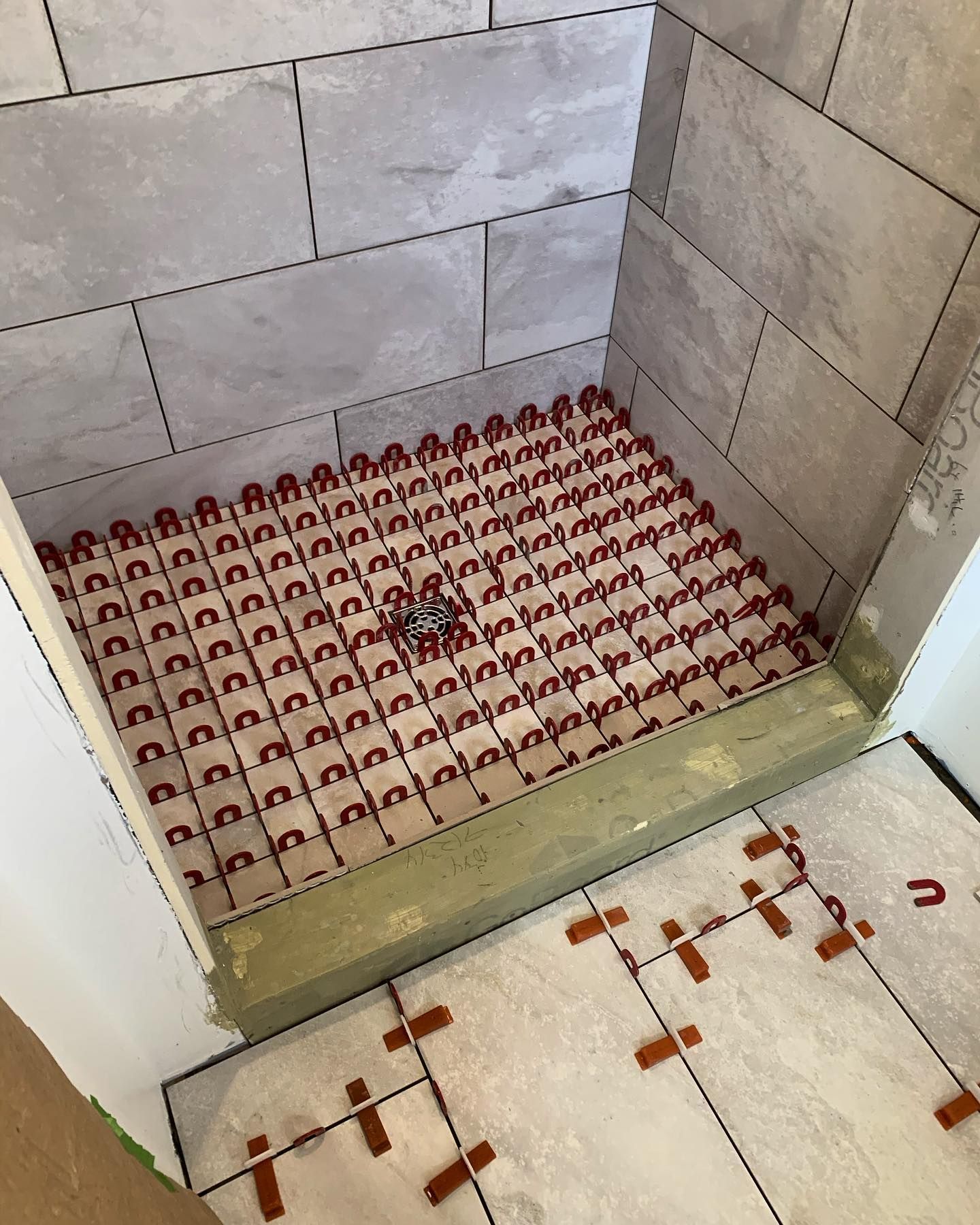 Shower stall under construction with tiles on walls and floor, red leveling clips visible.
