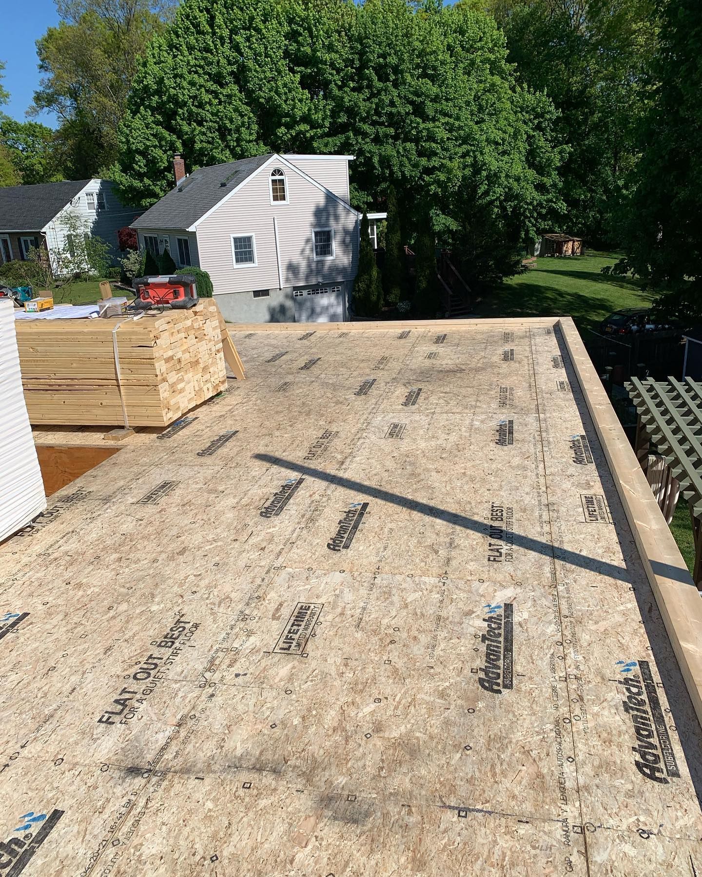 Rooftop construction: OSB sheathing laid on a flat roof with lumber and house in the background.