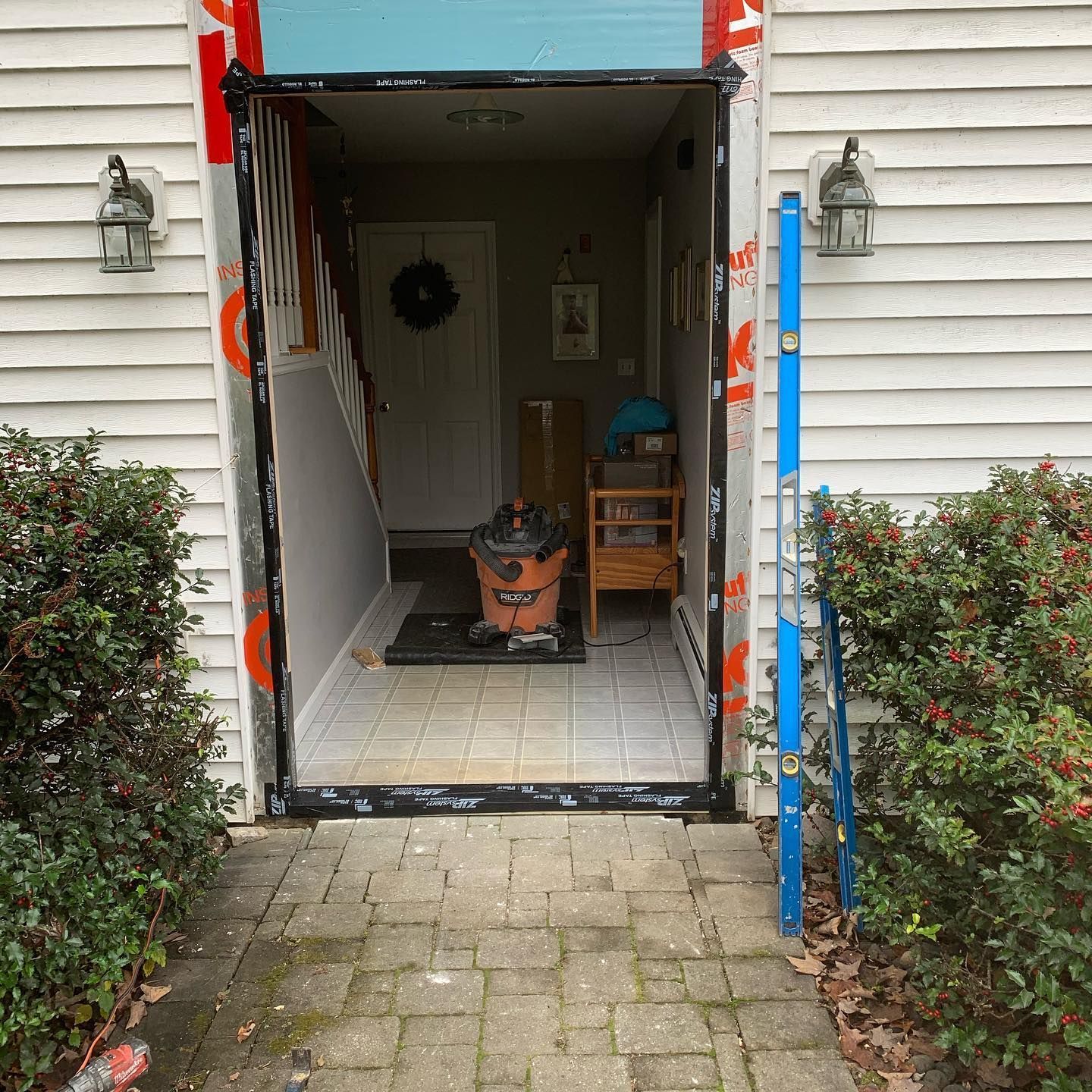 Exterior view of a house doorway with removed door frame, construction in progress; blue level leaning next to doorway.