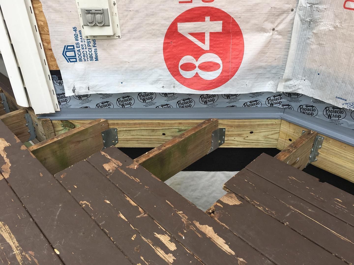 Wooden deck with stairs leading up; grey flashing; white and red paper on wall.