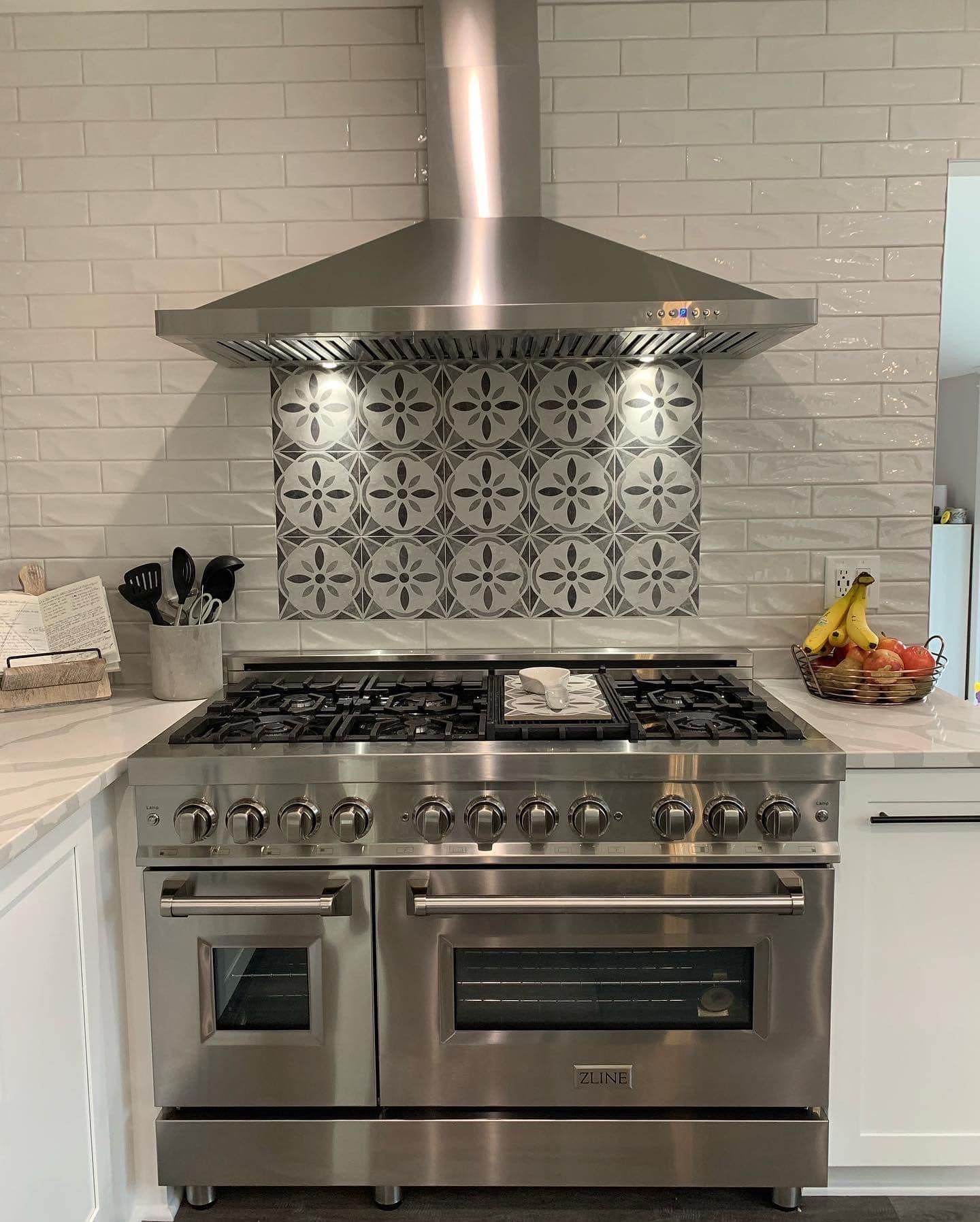 Stainless steel range and hood in a modern kitchen with patterned backsplash.