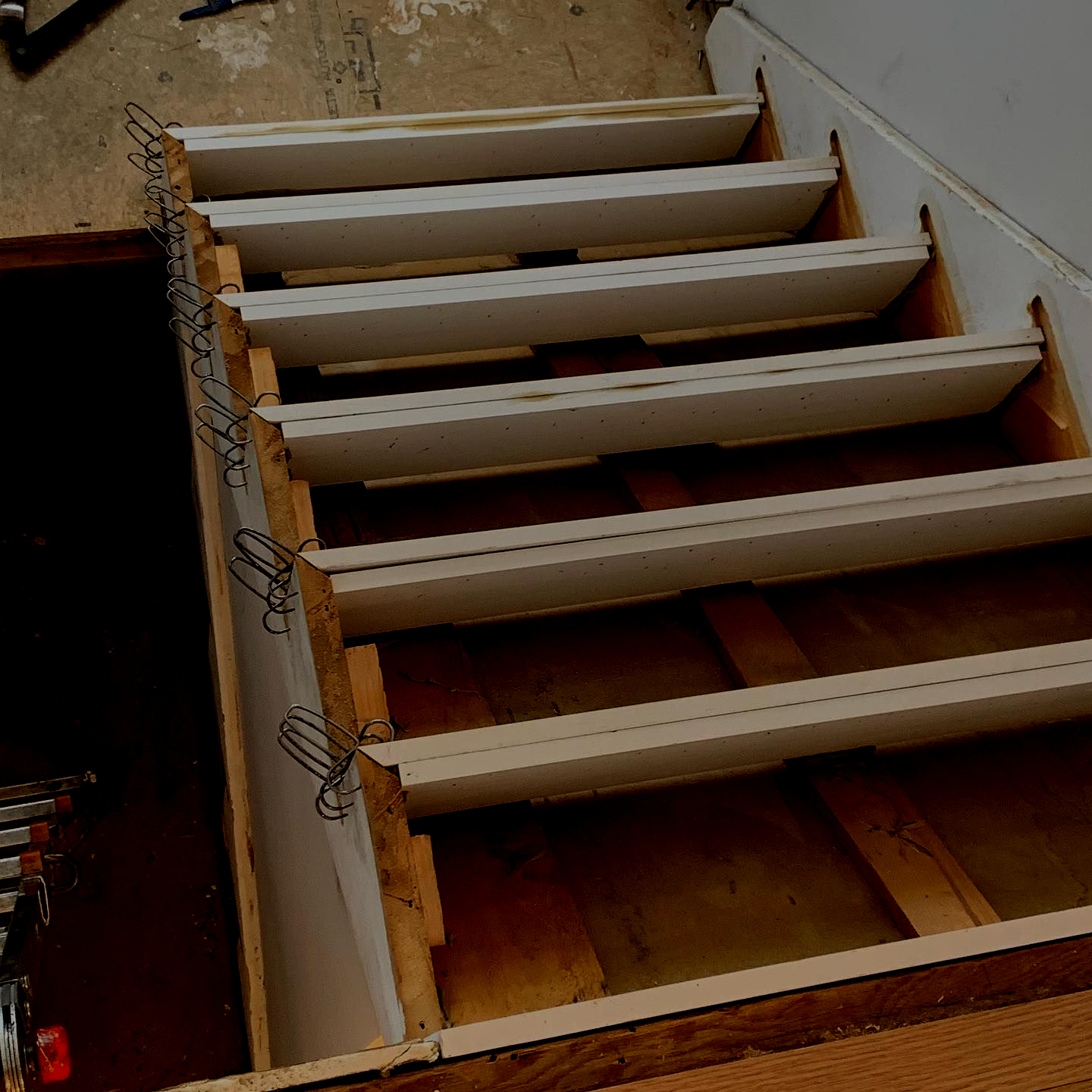 Staircase under construction, with white steps, clips, and exposed wooden supports.