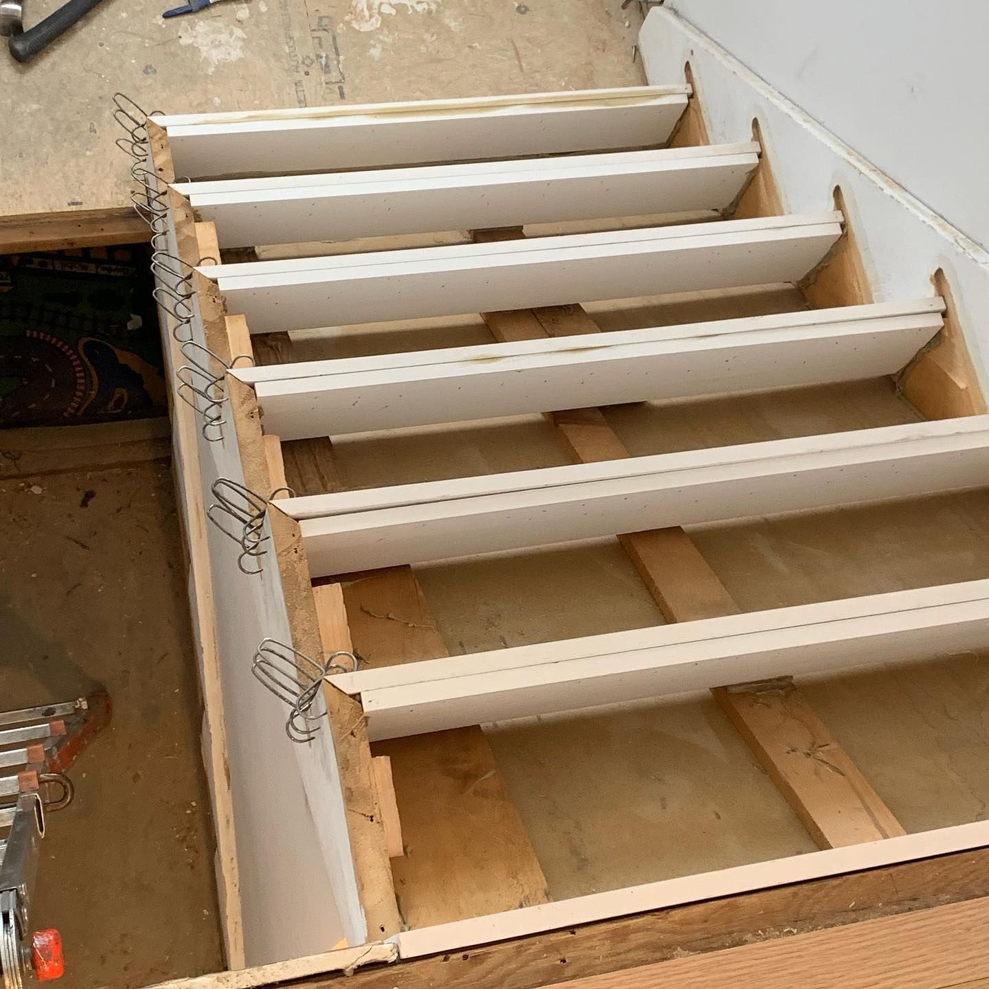 Staircase under construction: white steps, wooden supports, exposed framing.
