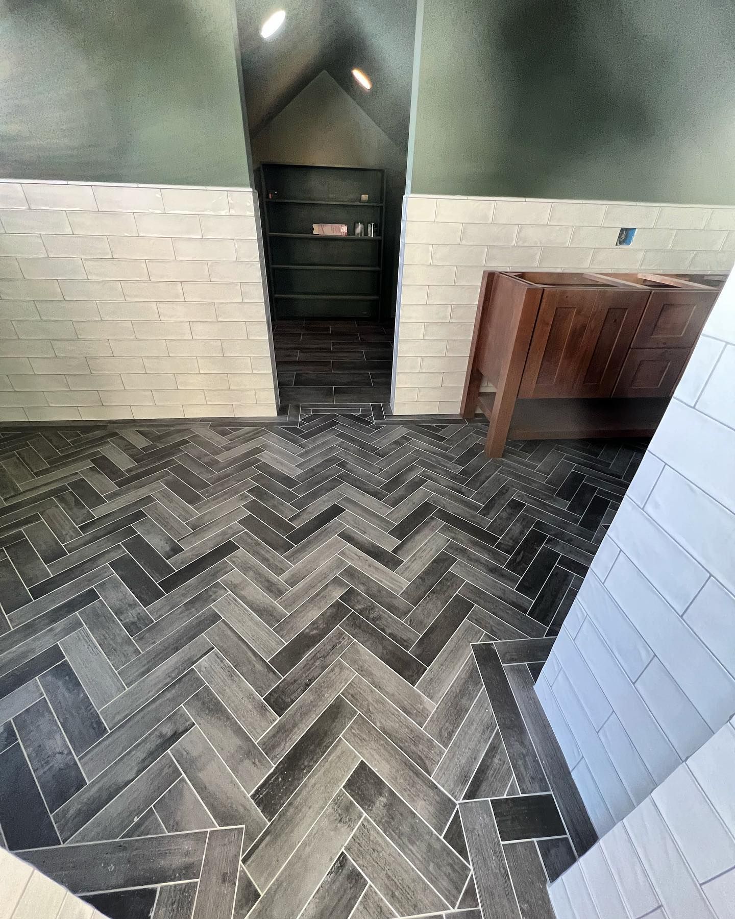 Herringbone tile floor with entrance to shelves, brick-like white walls, and a dark wooden vanity.