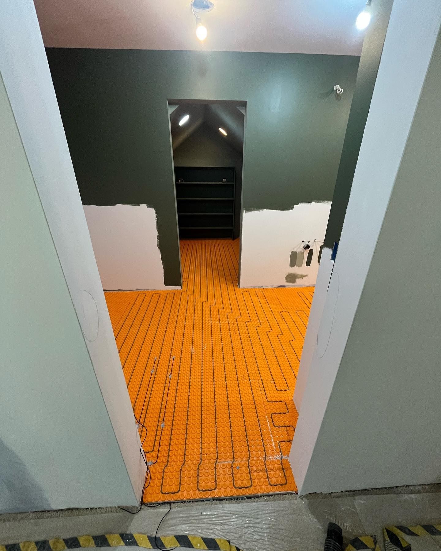 Orange floor heating system installation in a room with a doorway and green walls.