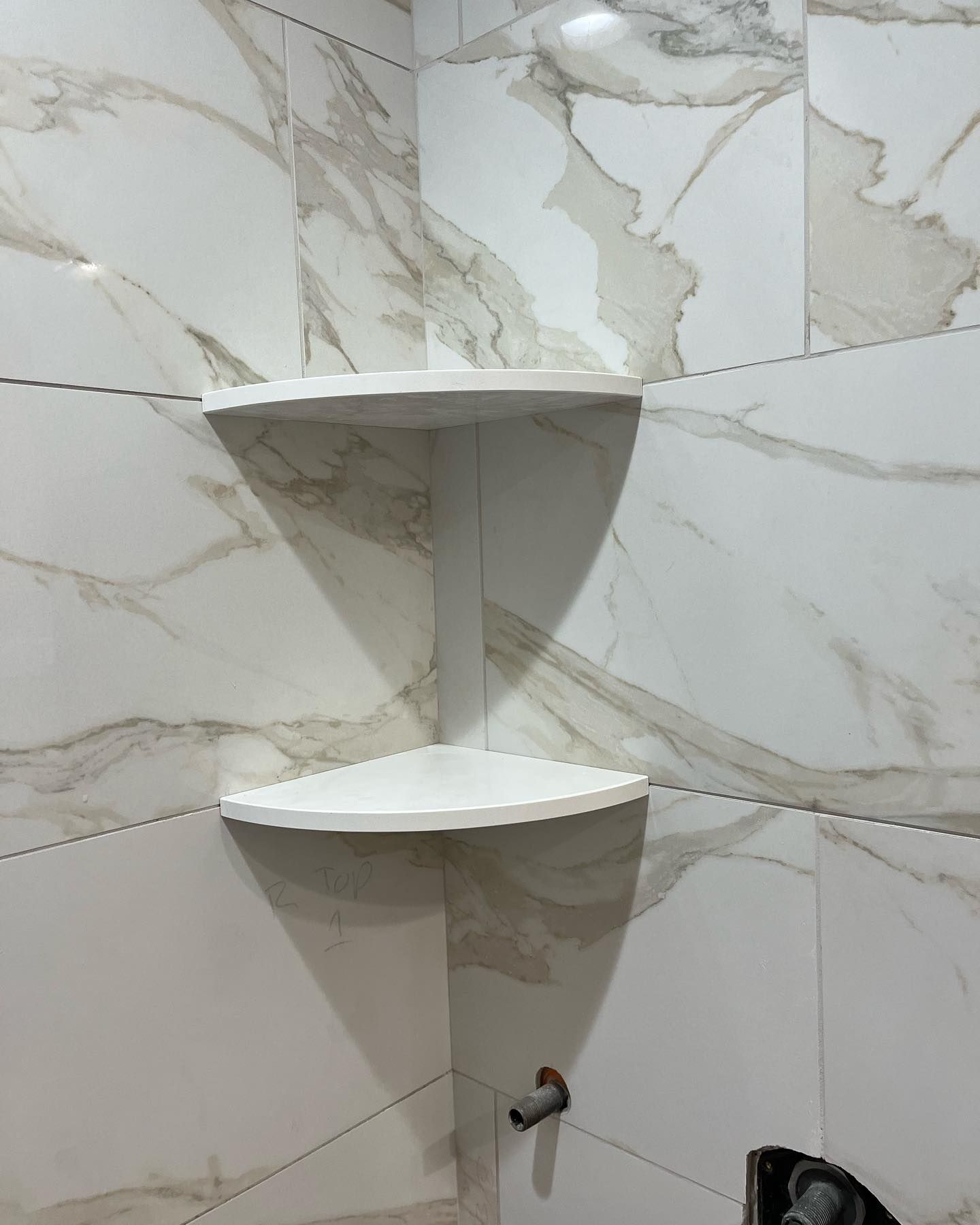 Two white corner shelves installed in a shower with marble-patterned tiles.
