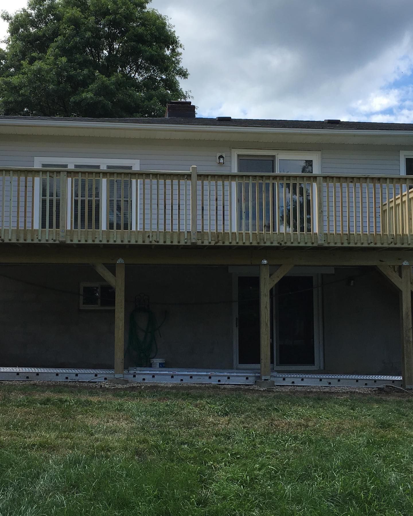 Two-story house with a wooden deck. Below, a doorway and grassy yard. Cloudy sky.