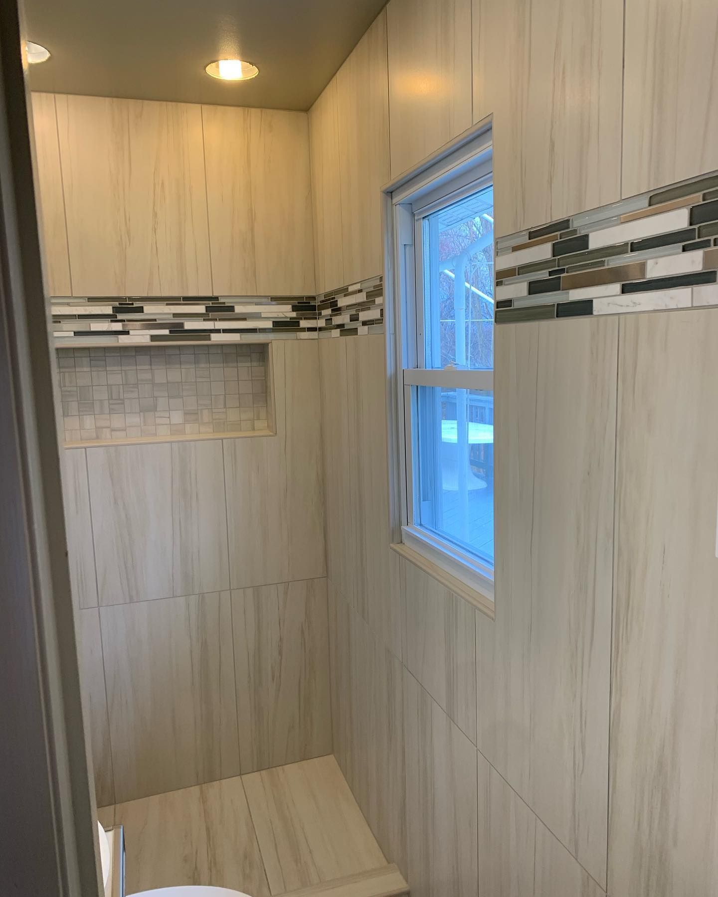 Small bathroom with light wood-look tile, mosaic accent, window, and recessed niche.