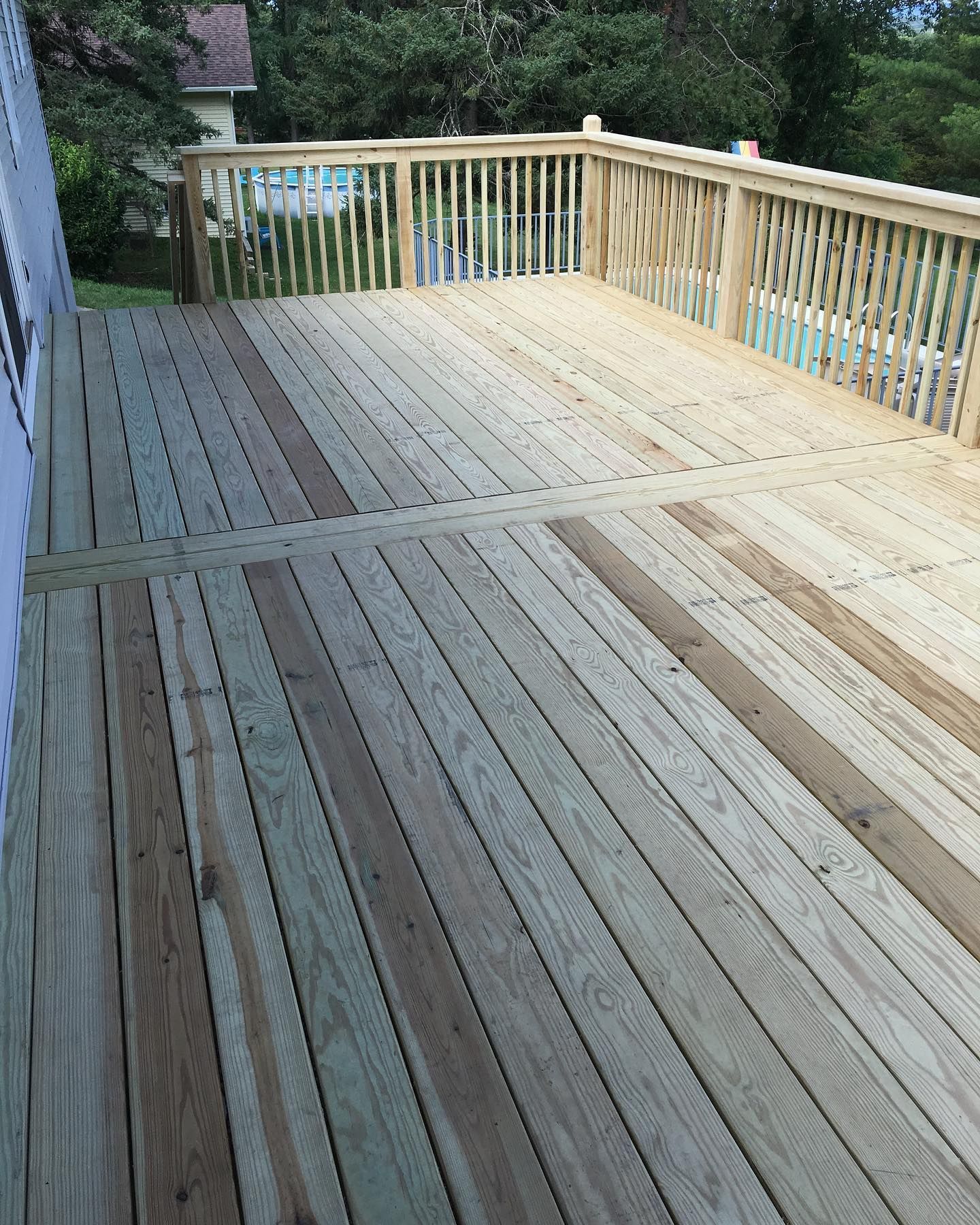 Wooden deck with railing, overlooking a backyard with a pool.