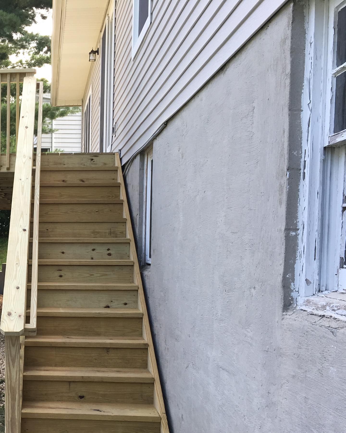 Wooden outdoor stairs lead up to a house with siding and a stucco foundation.