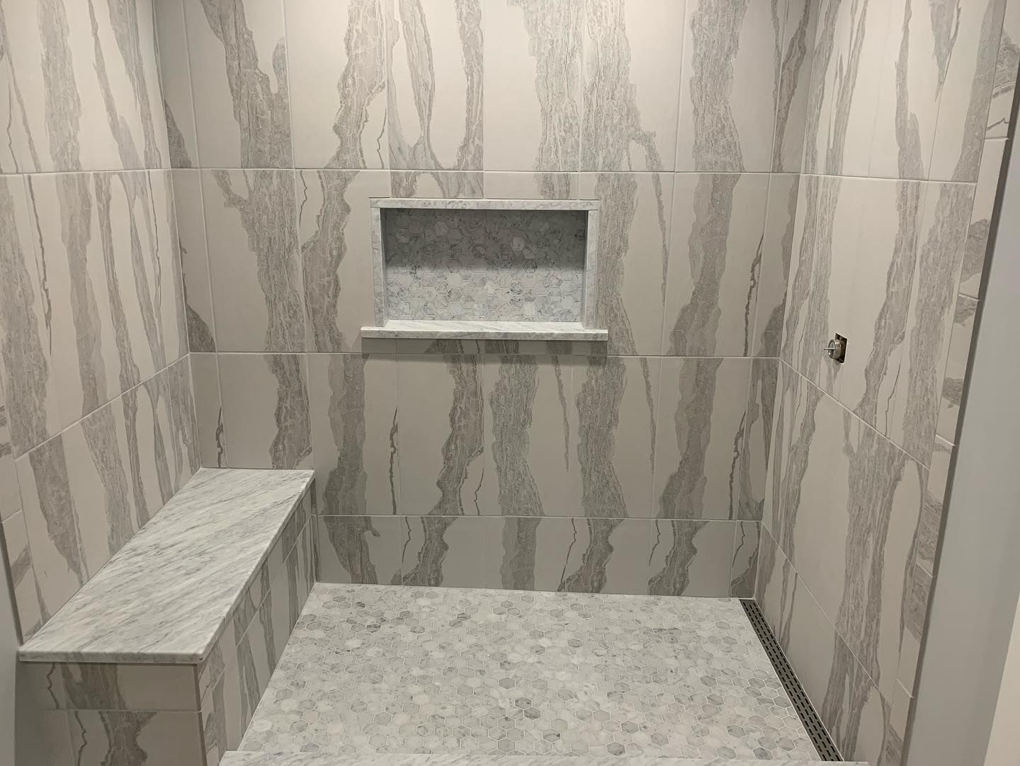Shower stall with white and gray marble-like tile; built-in bench, shelf, and pebble floor.
