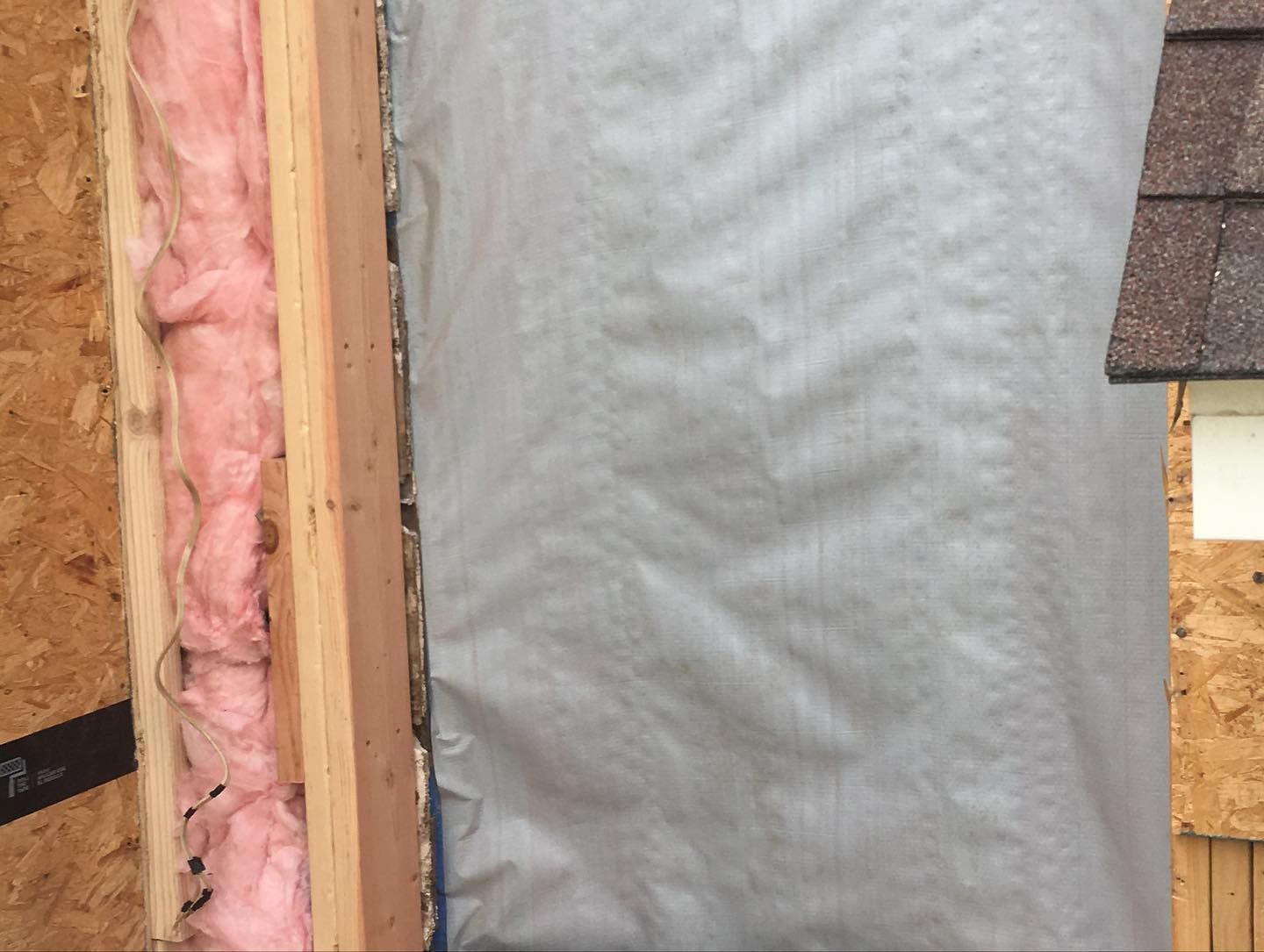 Wall construction showing pink insulation, wood framing, and a gray vapor barrier.
