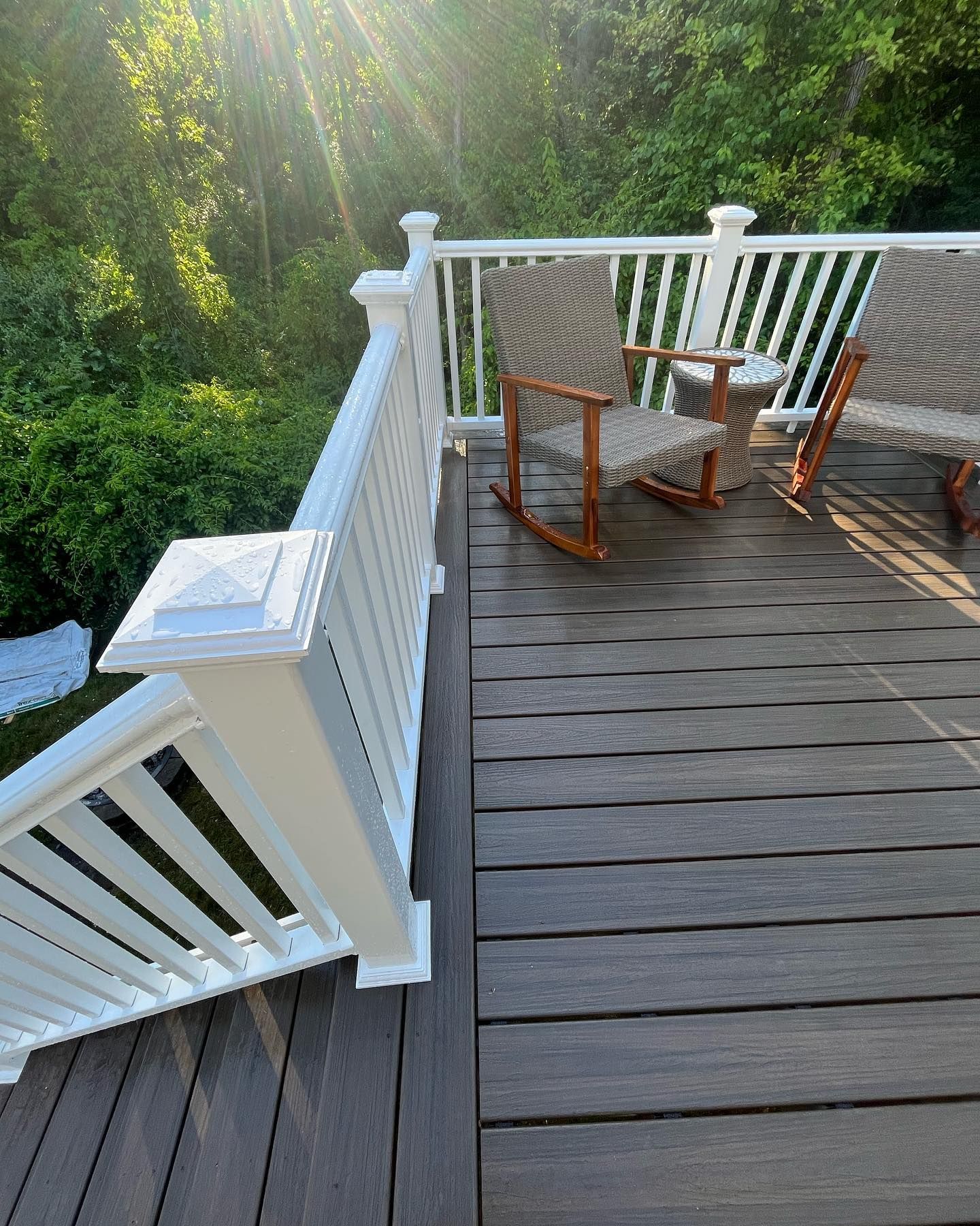 Wooden deck with white railing and two rocking chairs; trees in the background.
