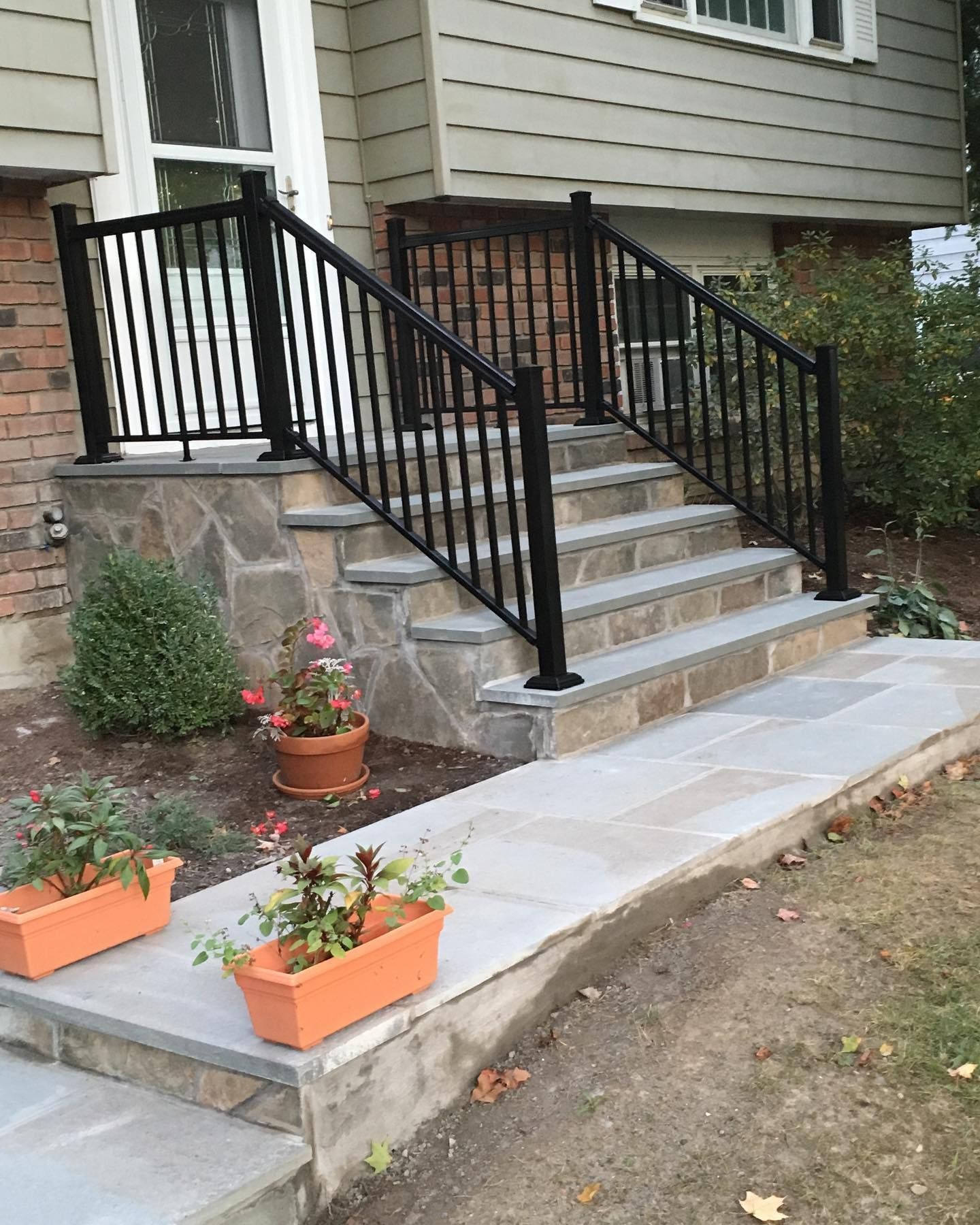 Black railing along stone steps leading to a house entrance, with flower planters.