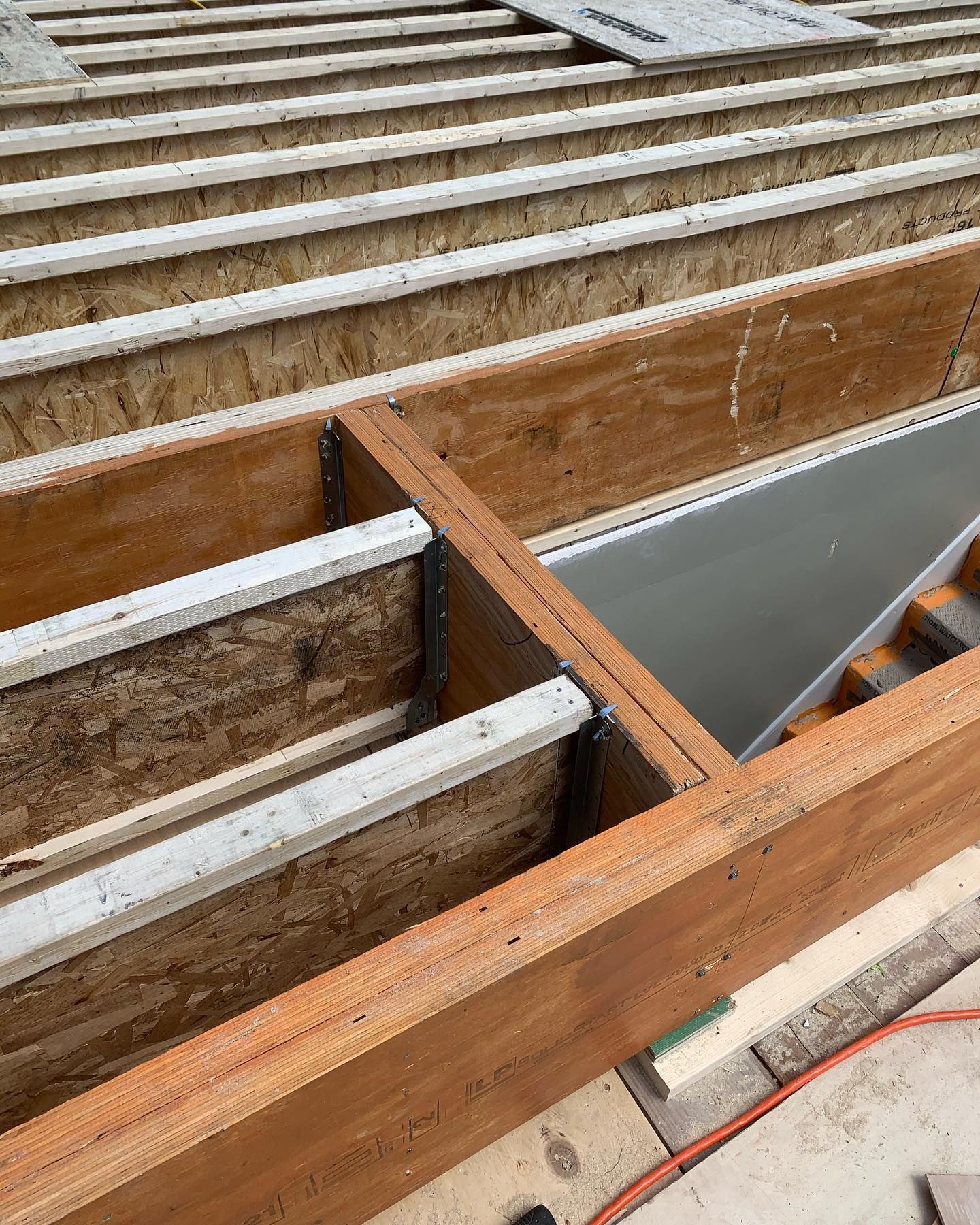 Wooden deck frame under construction with exposed joists and metal brackets.