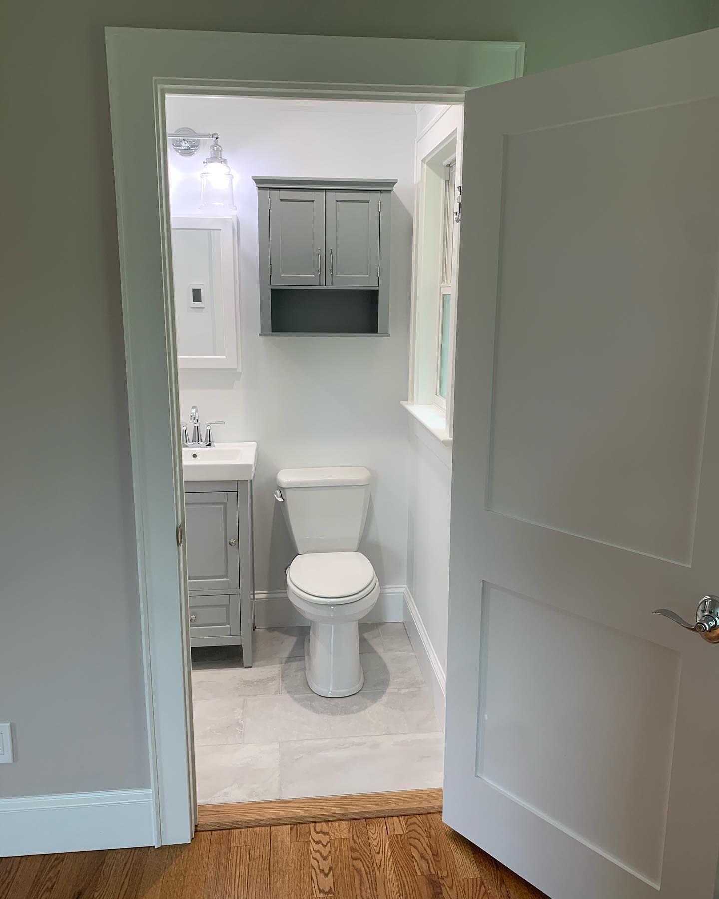 A small, renovated bathroom with gray fixtures, toilet, and vanity, viewed through an open doorway.
