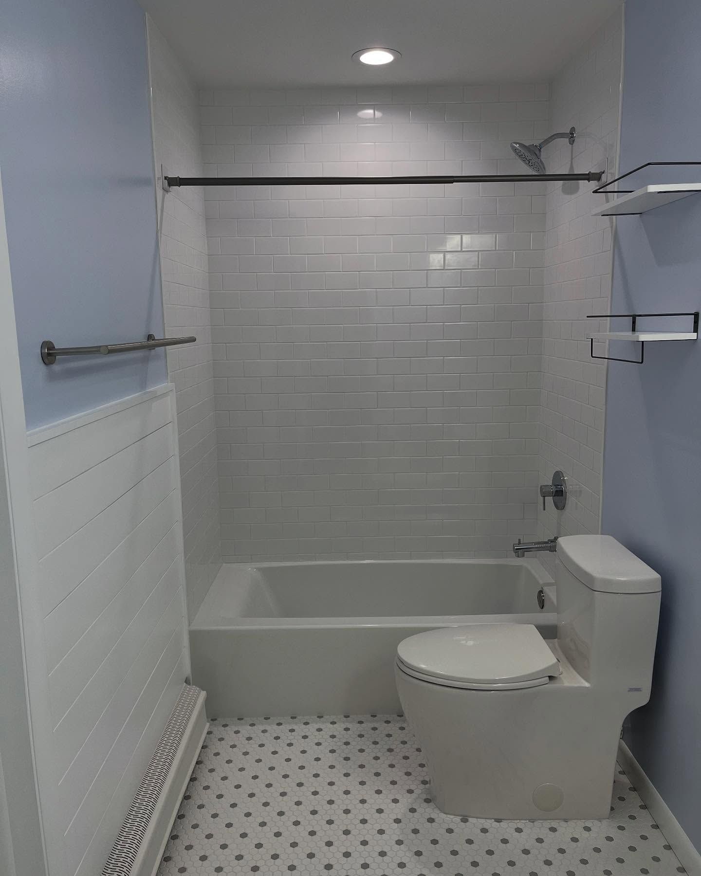 Small, white-tiled bathroom with a bathtub, toilet, and blue walls, featuring shelves and a towel rack.