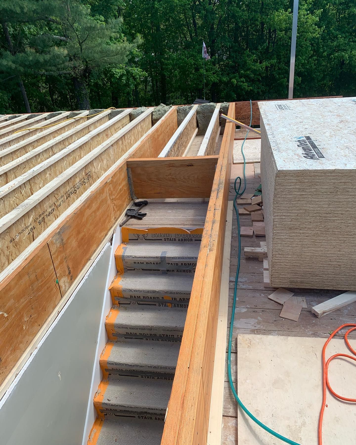 Construction site: wooden staircase leading to a higher level, with unfinished roof and surrounding lumber.
