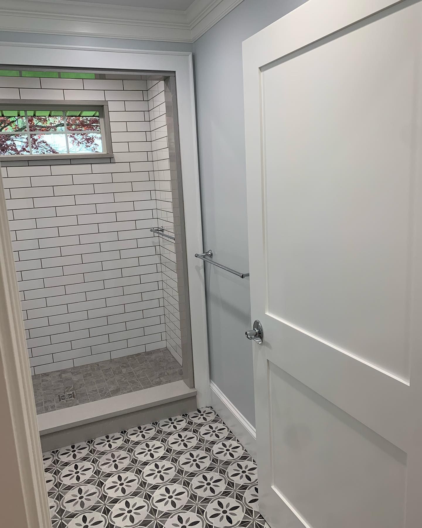 Bathroom with tiled shower, patterned floor, white door and gray walls.