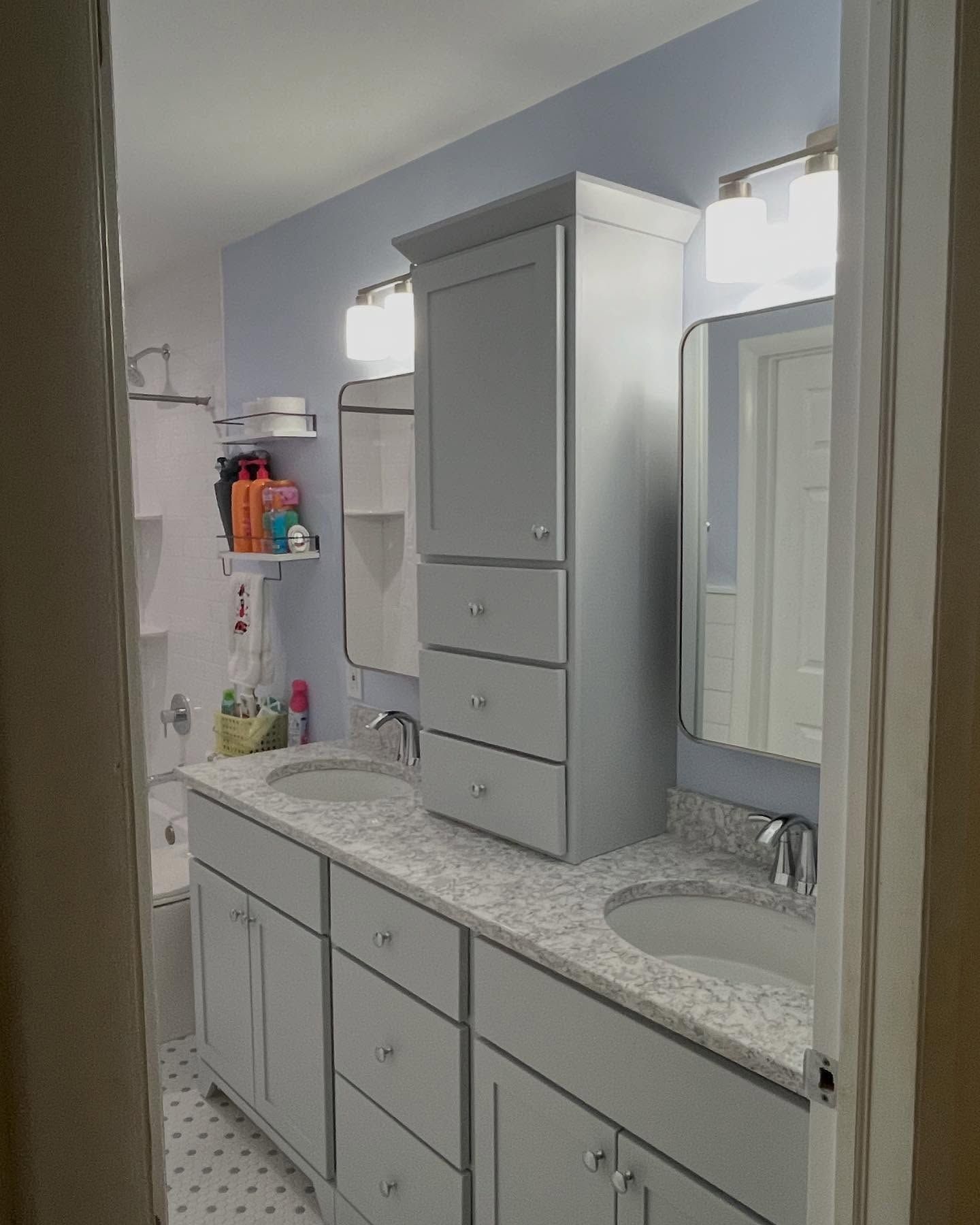 Bathroom with double vanity, a tall cabinet, light blue walls.