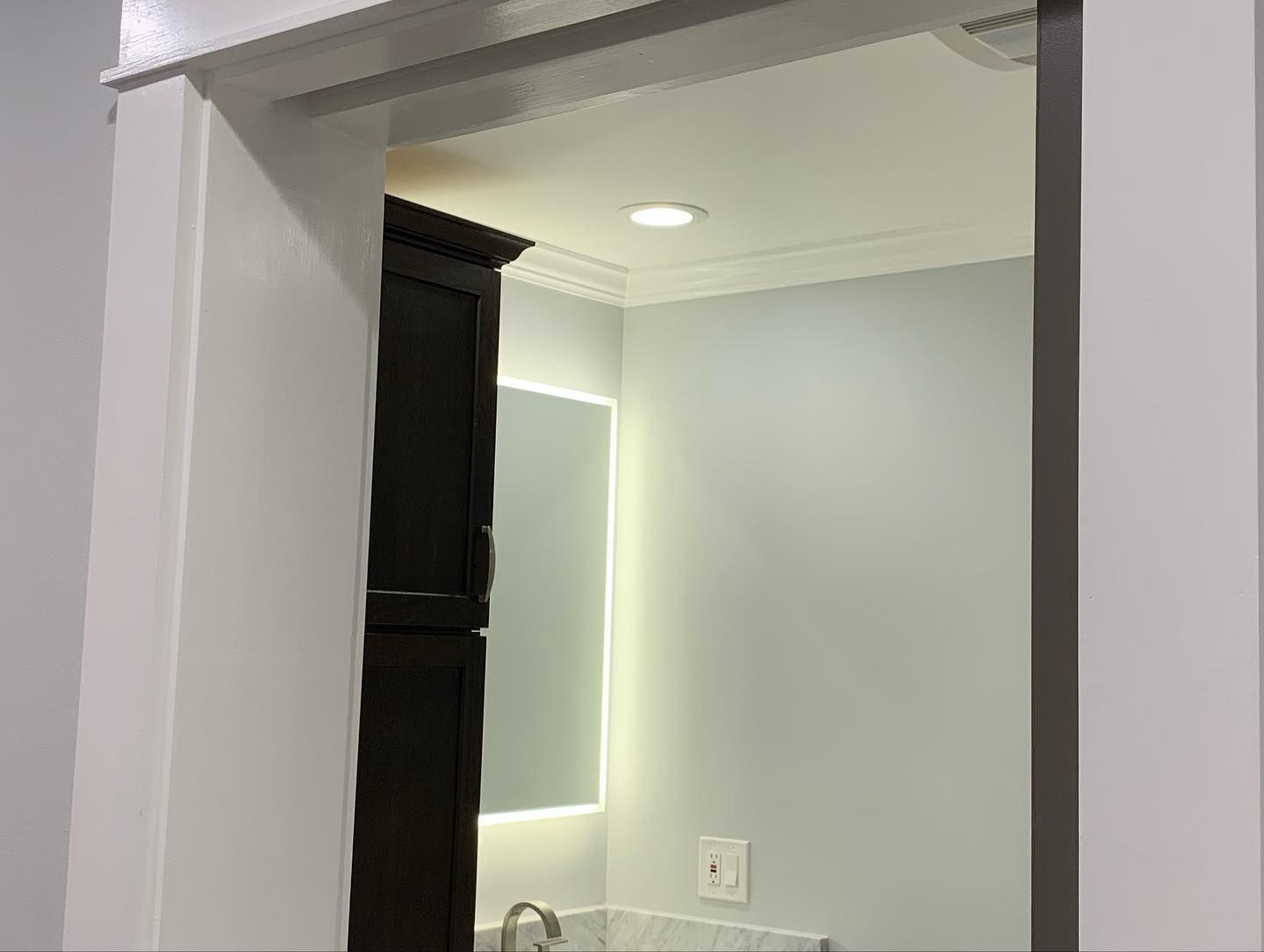 Bathroom doorway; white trim, light blue walls, dark cabinet, mirror, and light.