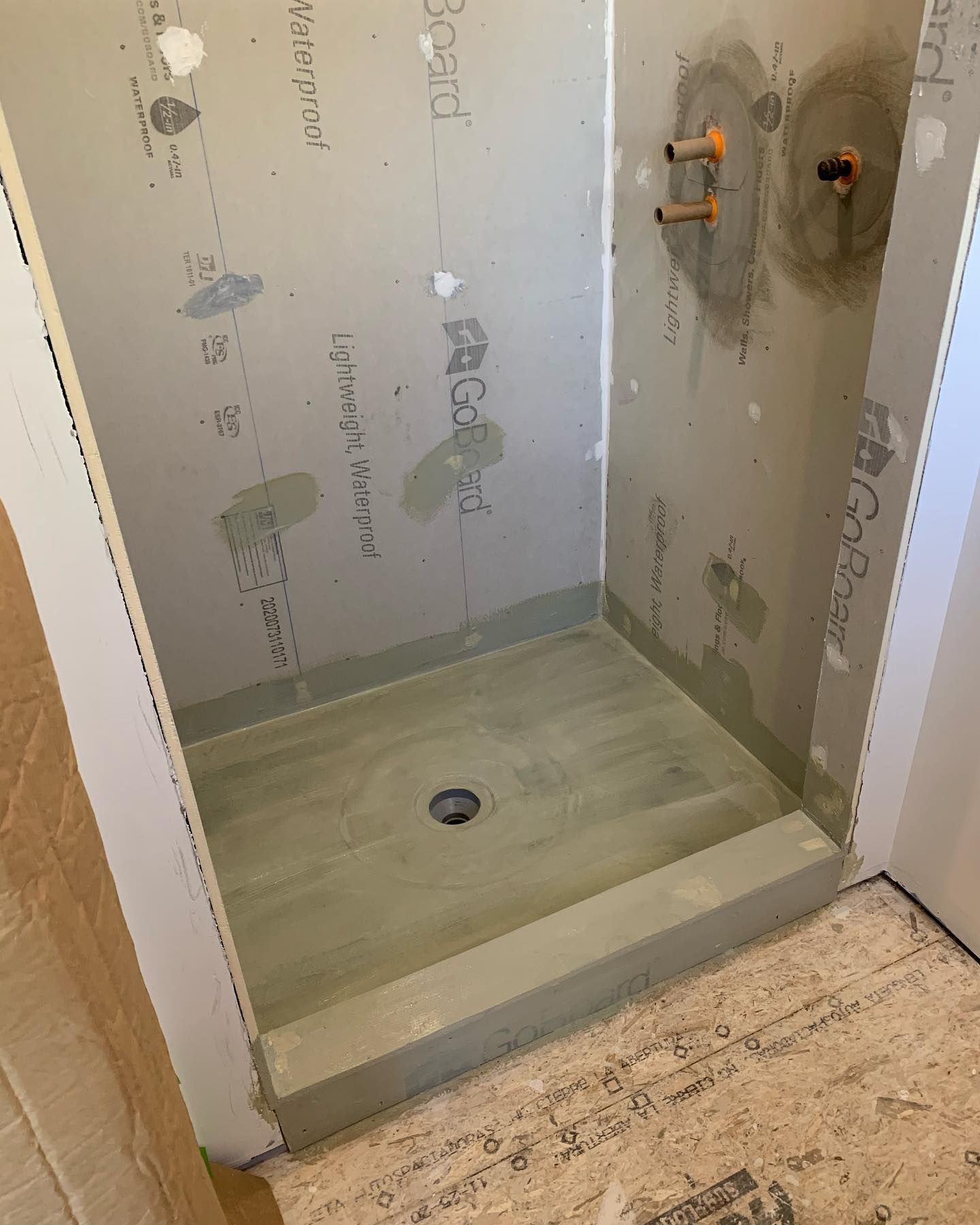 Shower stall under construction, with gray cement board walls and base, and copper pipe fixtures.