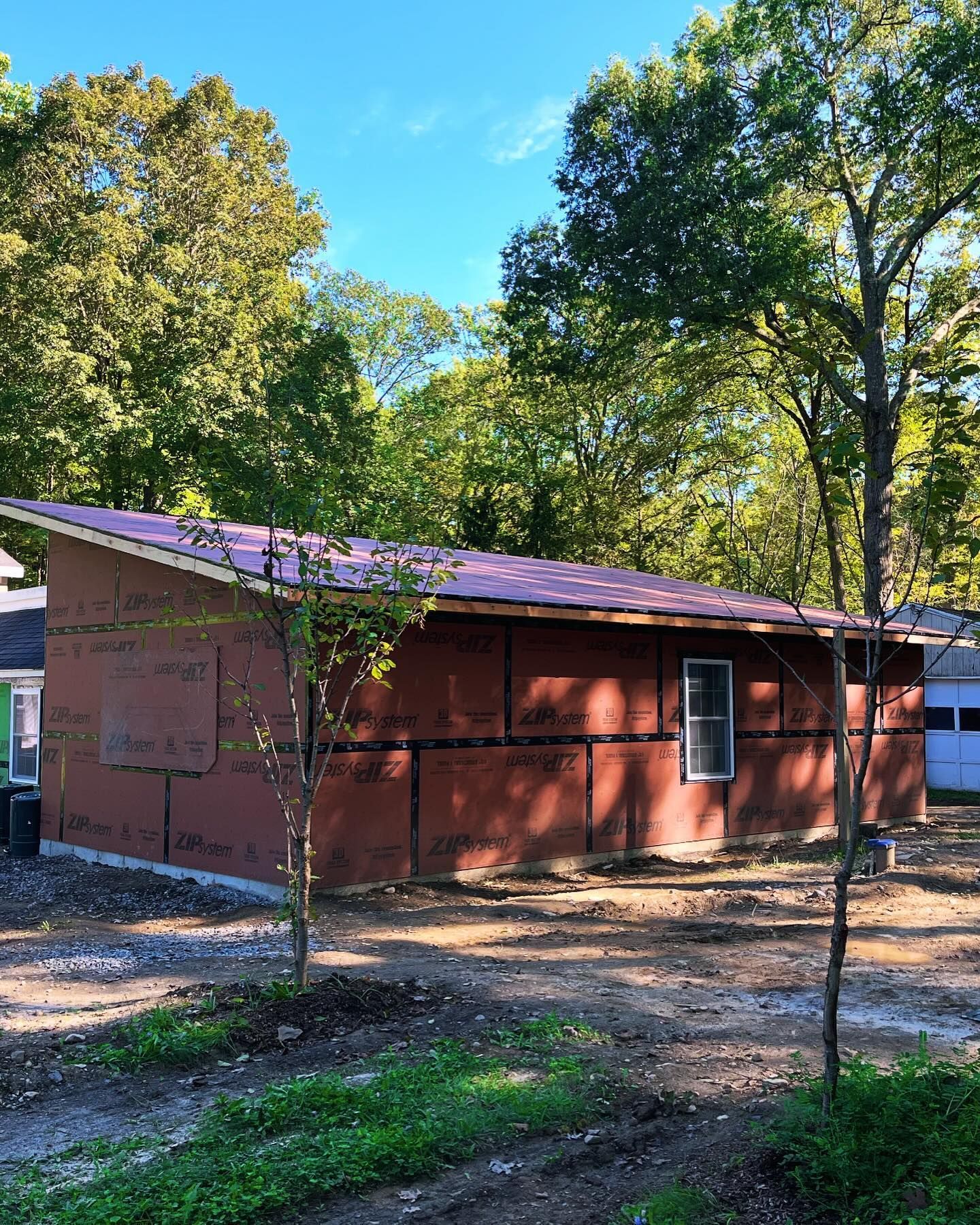 Brown building under construction with angled purple roof, small window, trees in the background.