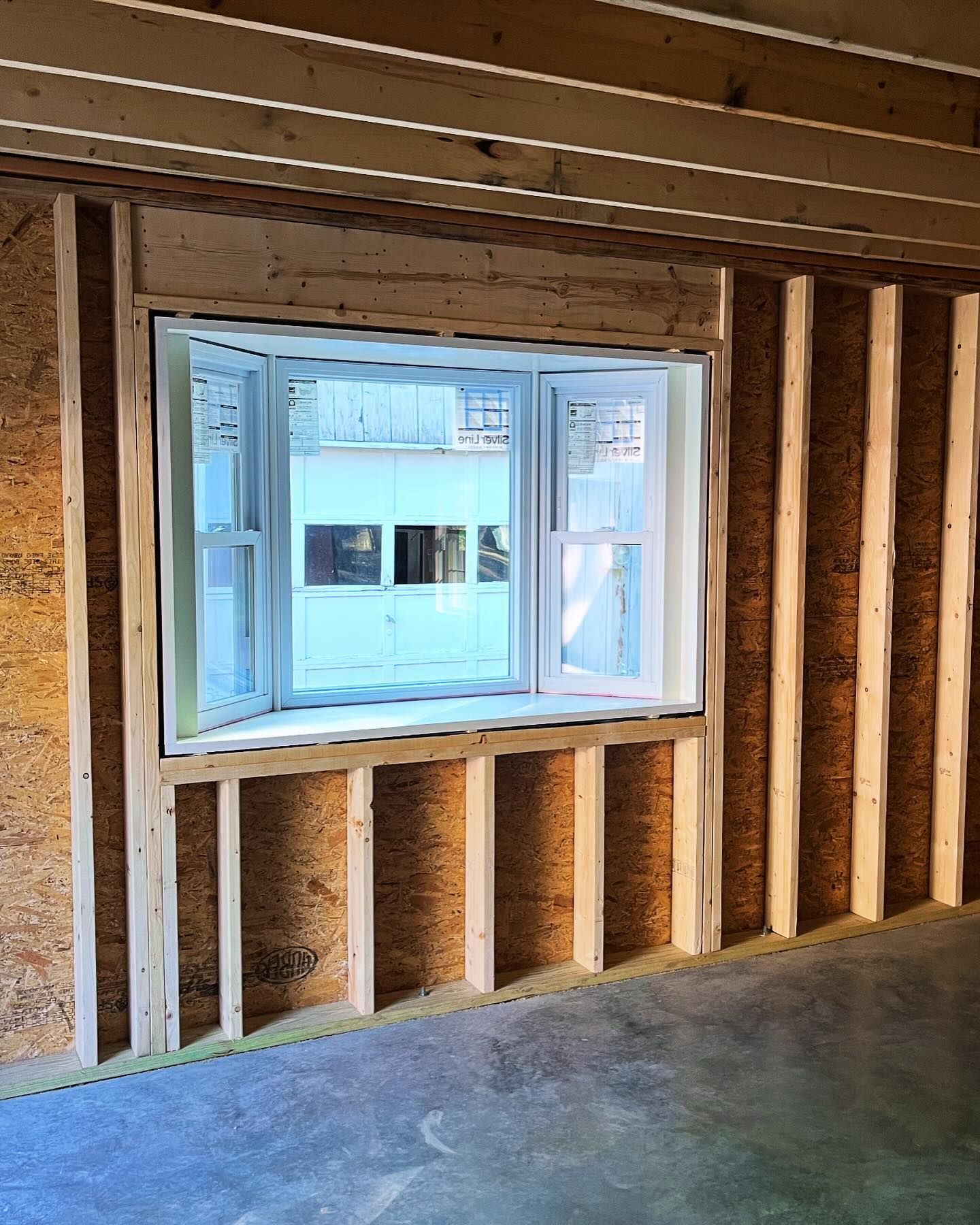 Bay window in a framed, unfinished interior. The window is white, and the walls are bare wood.