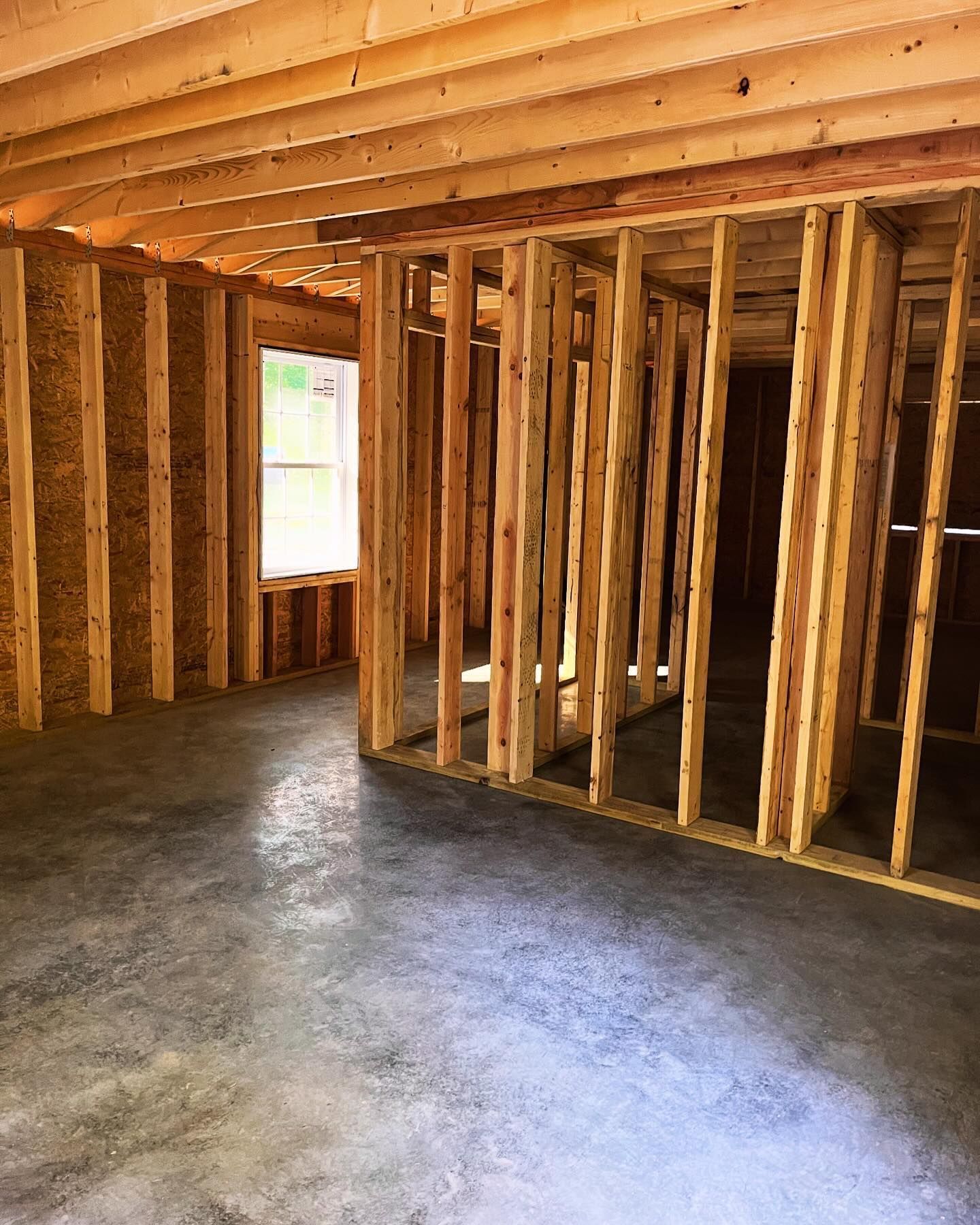 Interior of a building under construction, showing exposed wooden framing and a concrete floor.